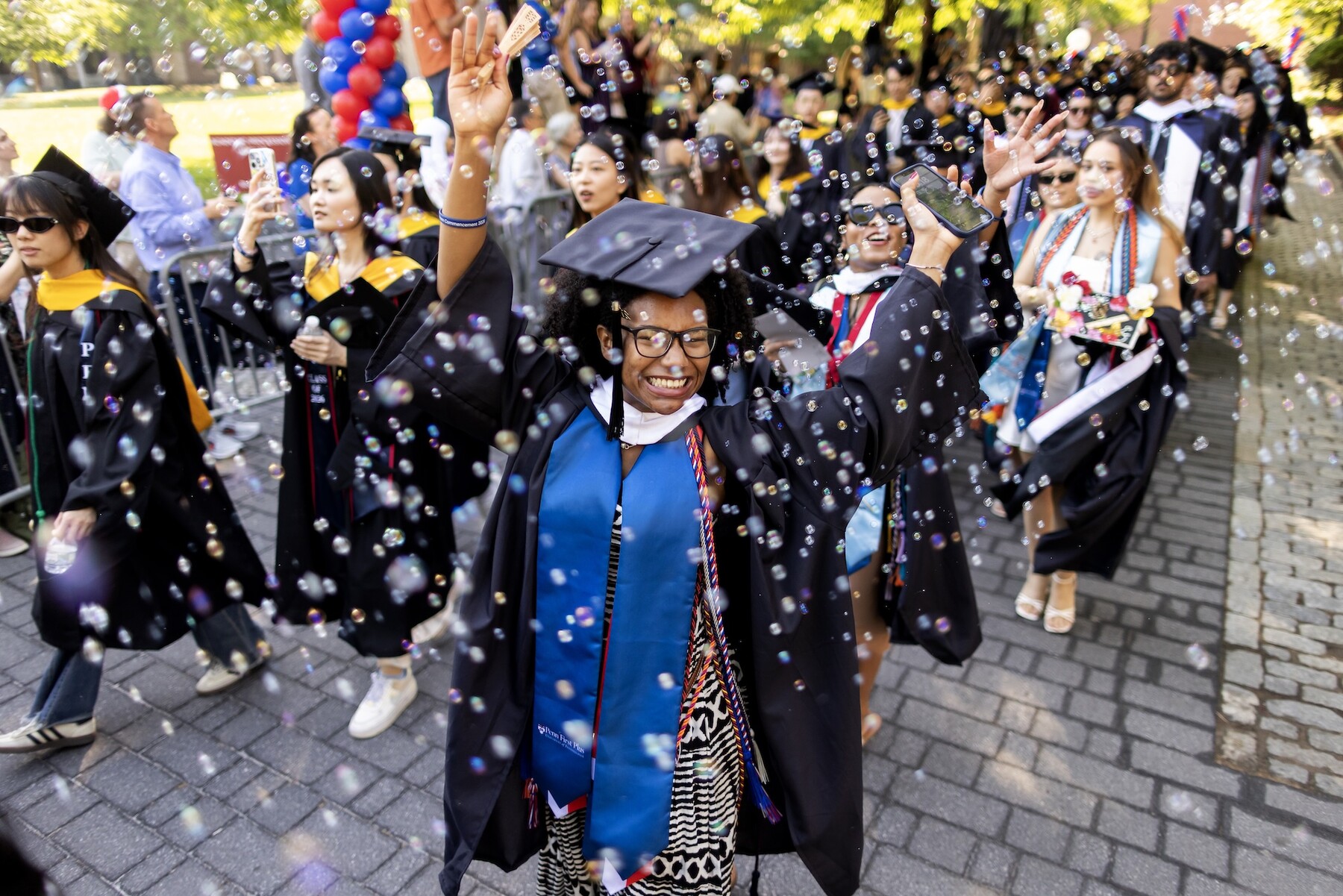 Students celebrating amongst bubbles while walking down Locust Walk towards Commencement.