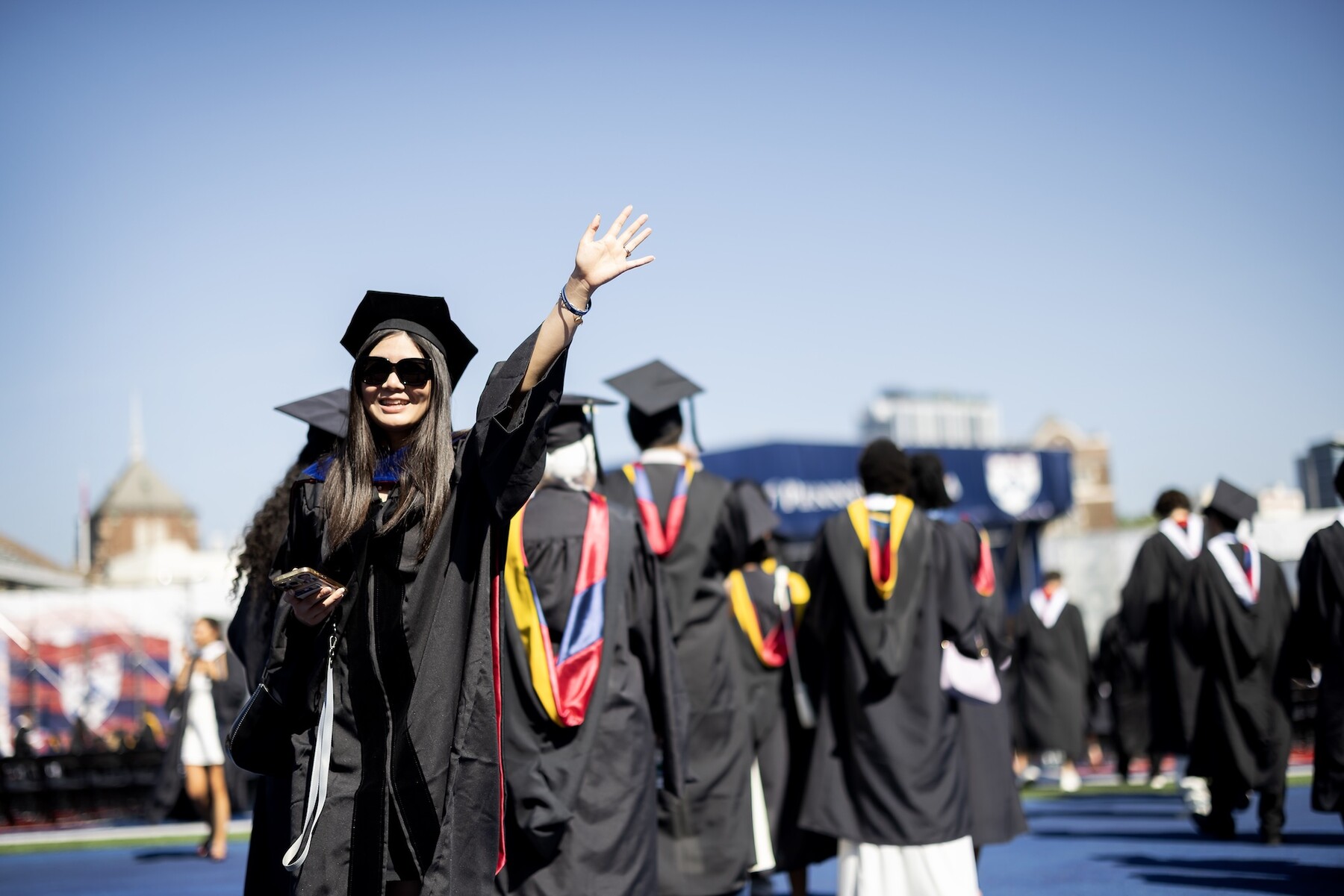 A student waving while walking onto franklin field for commencement.