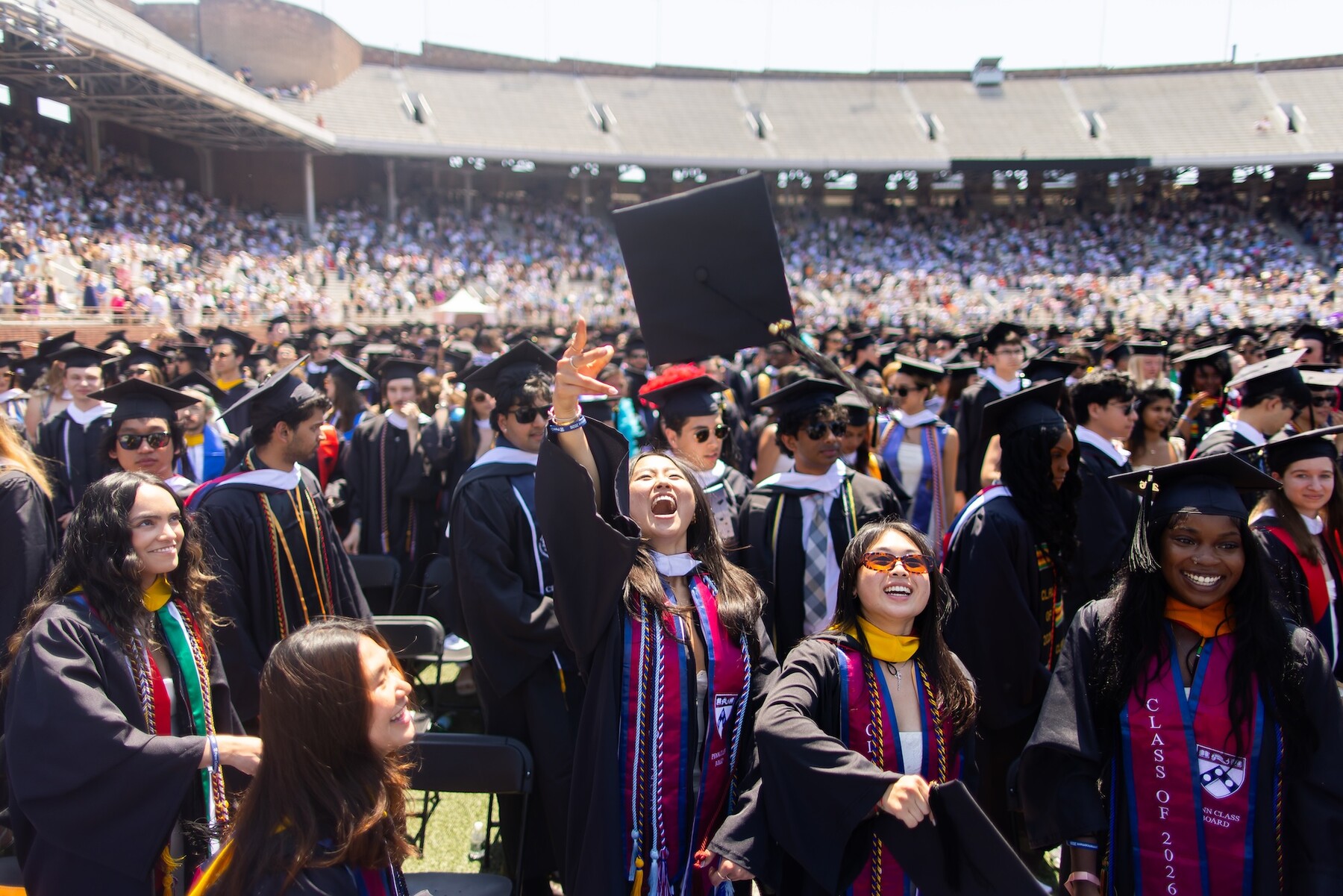A graduate tossing their mortarboard into the air in the crowd on Franklin Field.