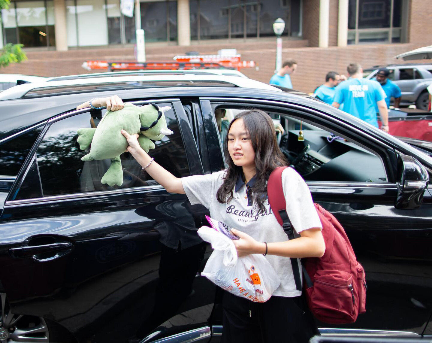 A student grabbing a stuffed animal out the window of their car during Move-In.