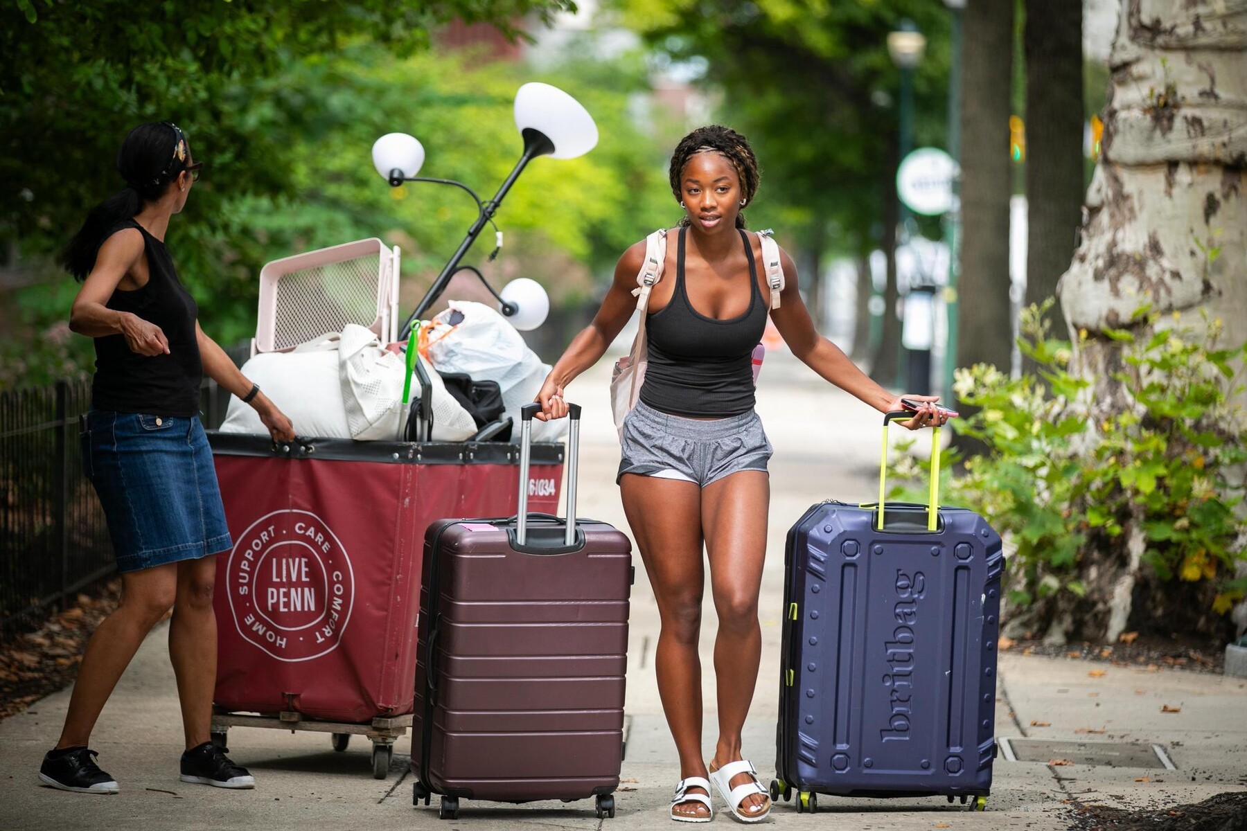 A student with two suitcases walking into a dorm during Move-In.
