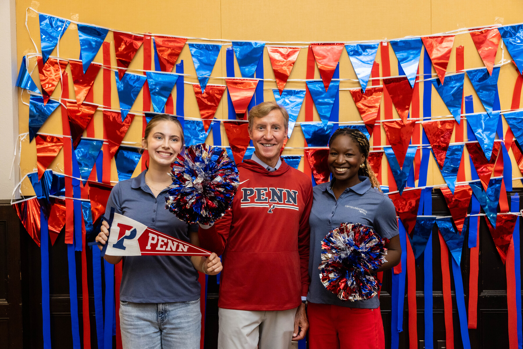 Penn President J. Larry Jameson standing with two students posing with cheer props.
