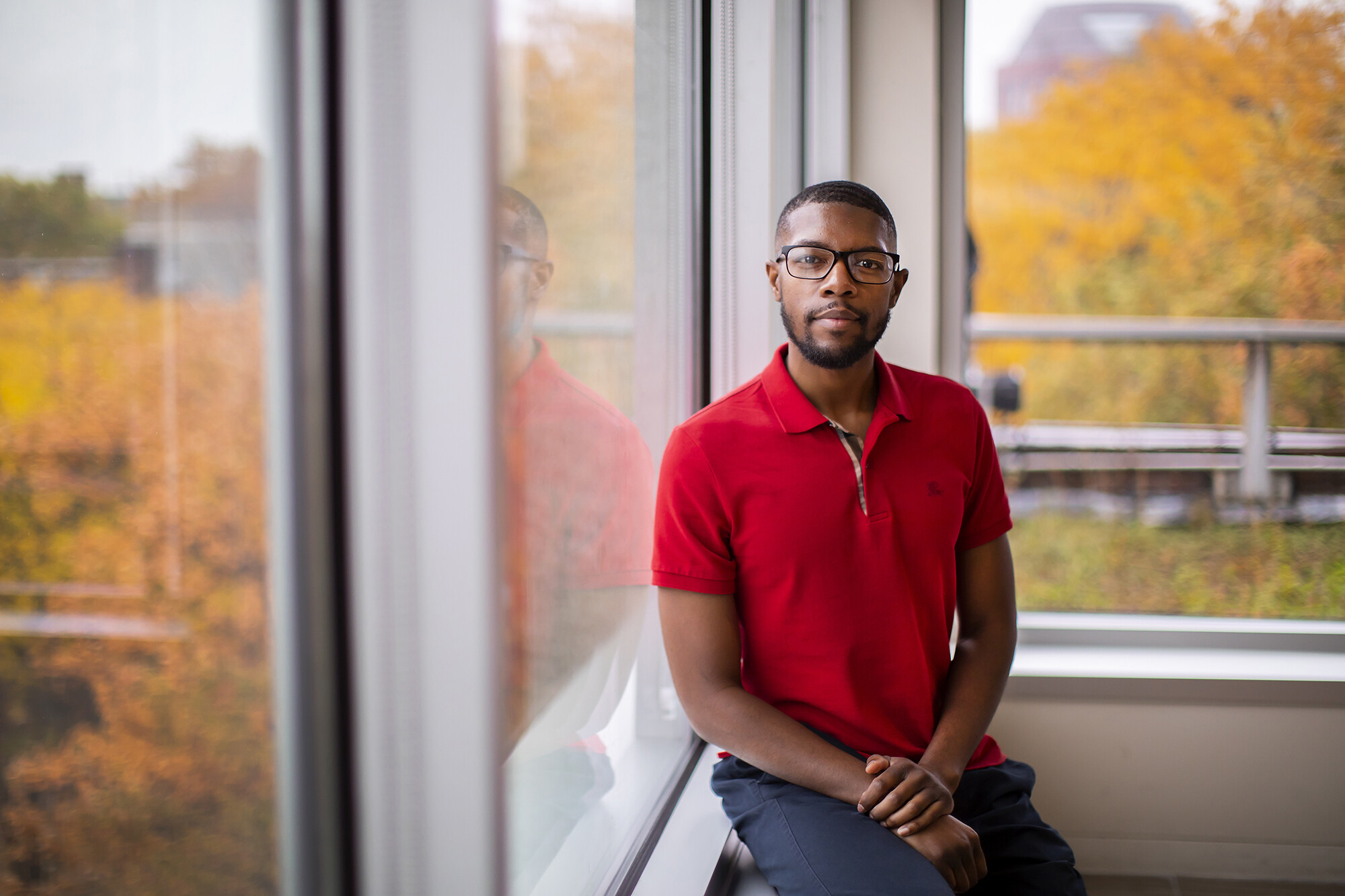 JD Goins, seated by a window and surrounded by colorful Autumn trees.