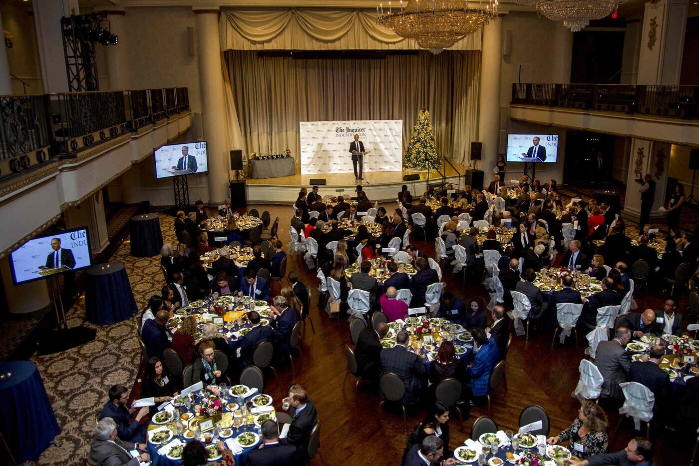 An overview of people eating dinner at 12 tables in a ballroom 