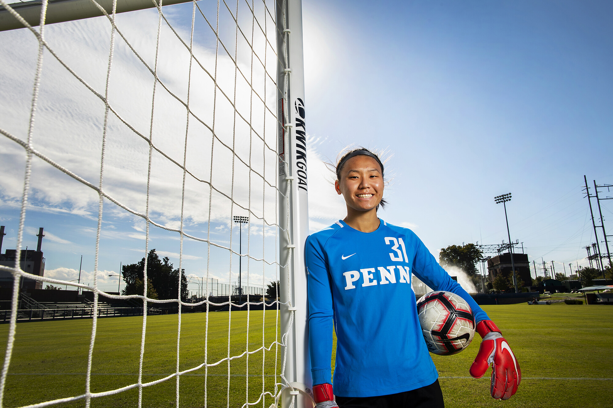Qu stands in portrait photo next to goal post on Rhodes Field