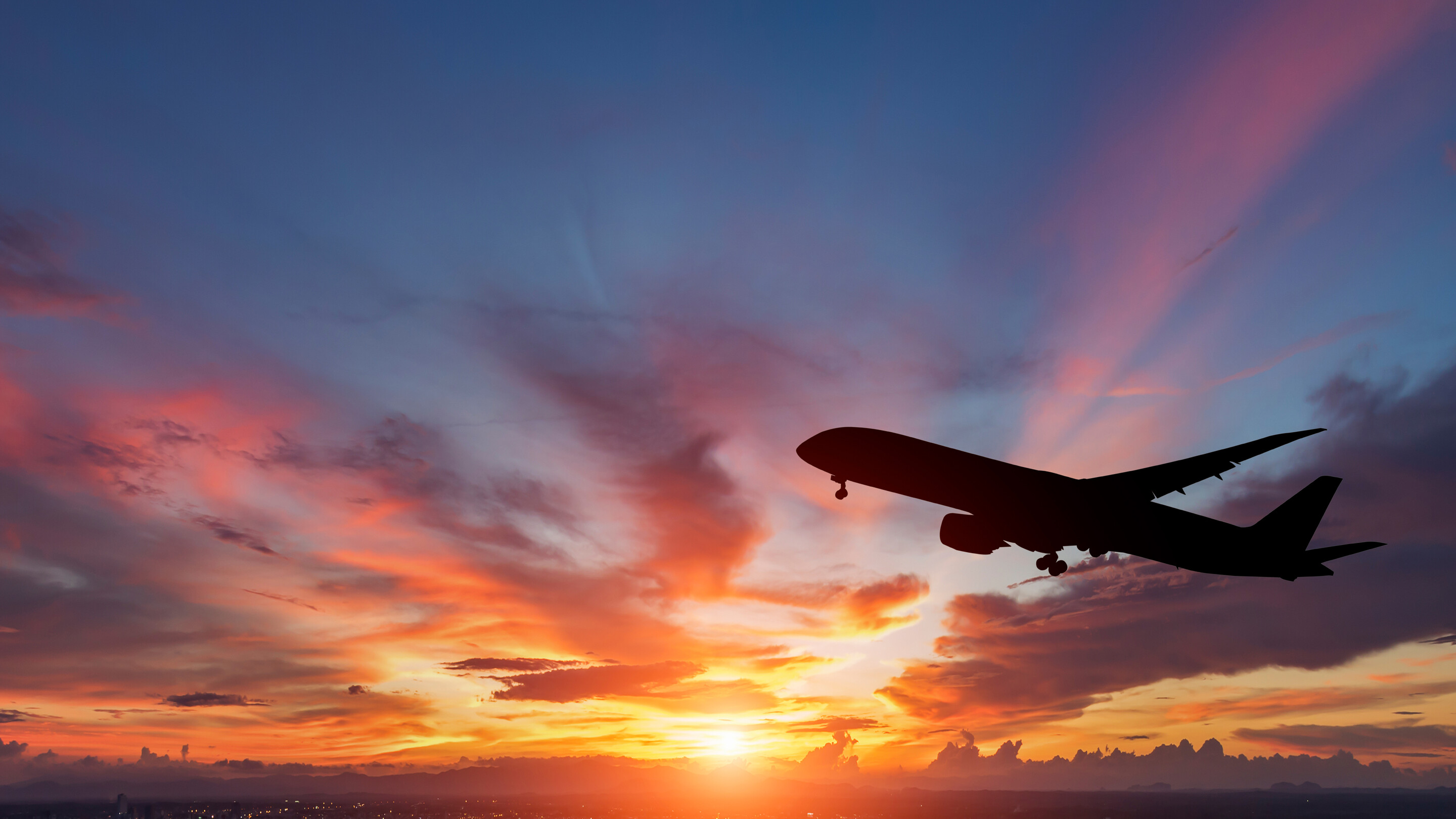 Silhouette of an airplane flying through a sunset 