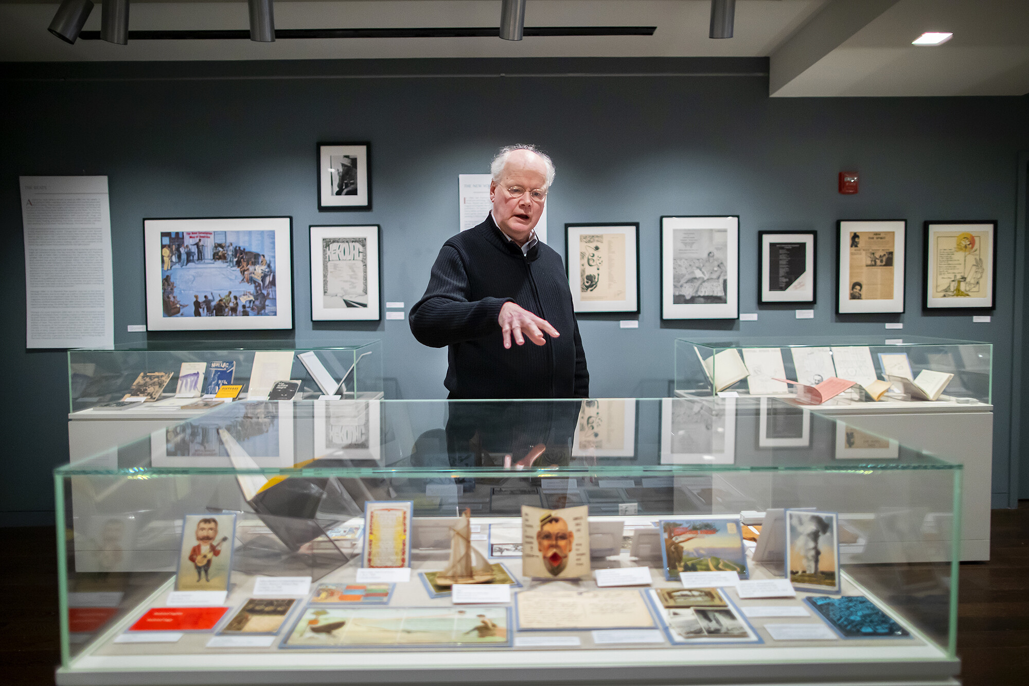 Librarian standing behind museum display case holding several postcards.