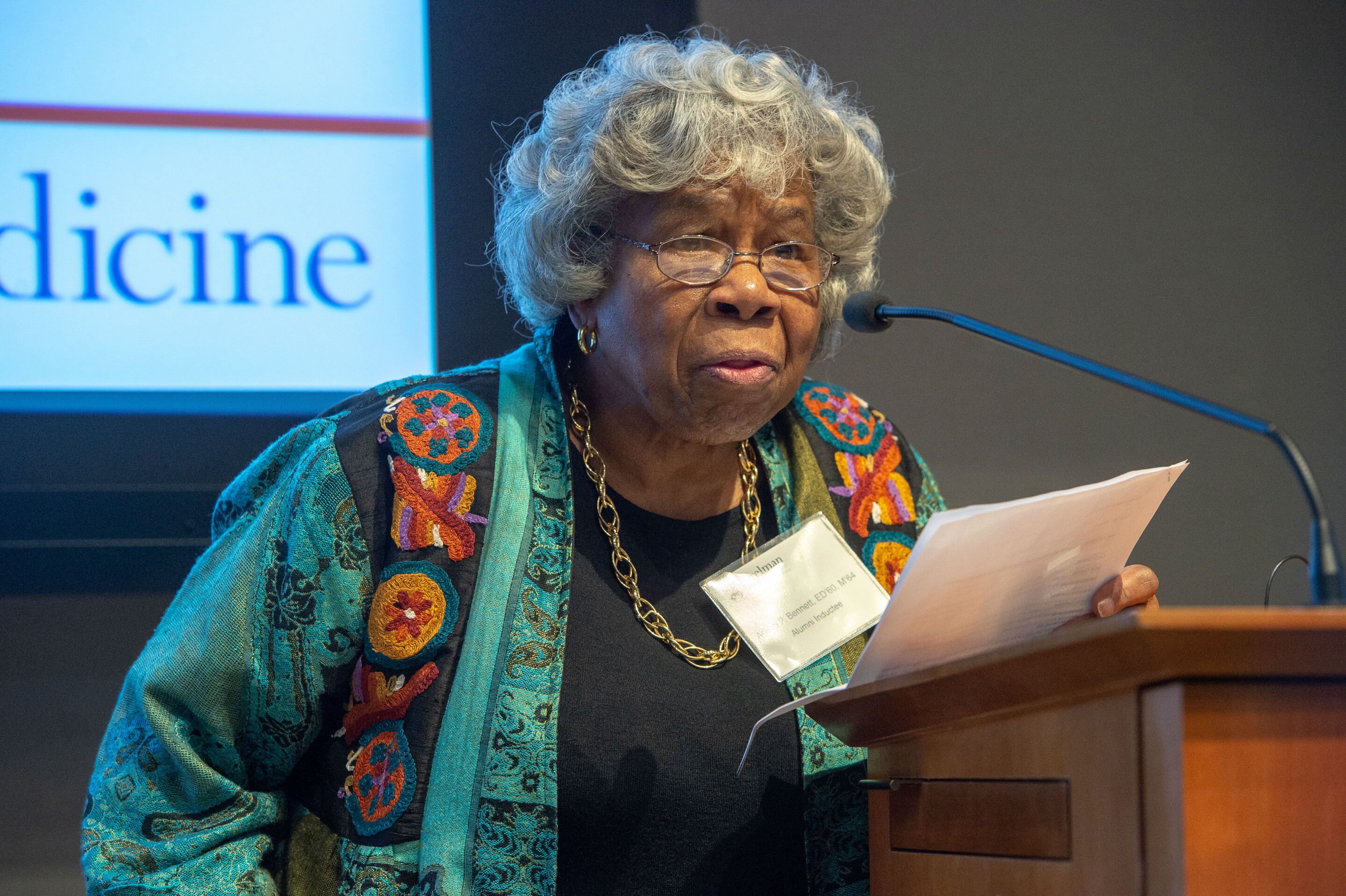 African American woman in a green sweater and black shirt standing at a podium