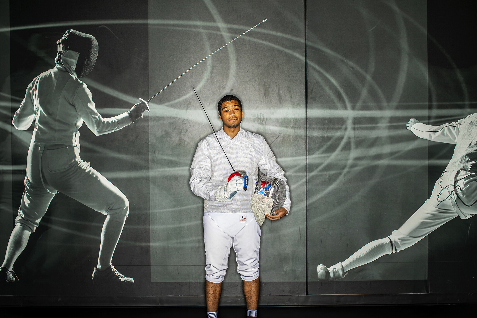 Fencer Julian Merchant poses standing with his sword and mask in Hutchinson Gym.