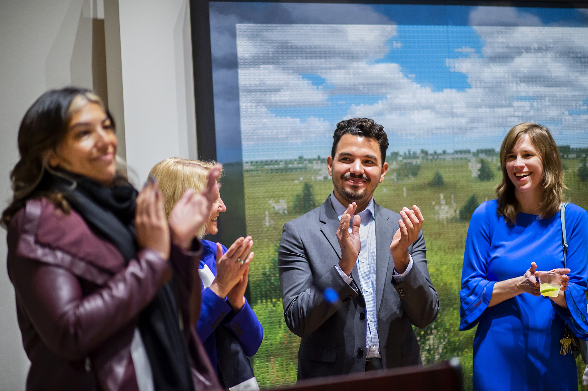 Four people standing in front of a painting, clapping and looking at each other. 