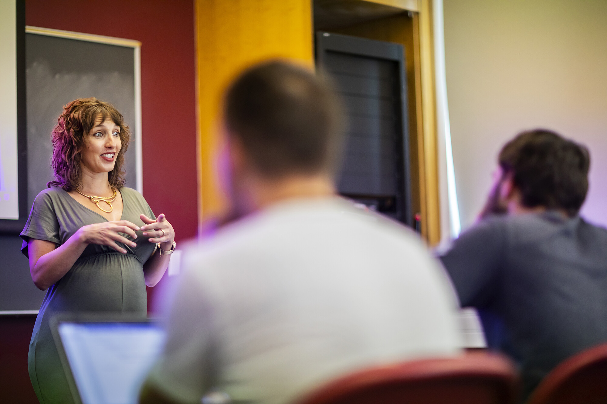An instructor gestures and speaks to students in a classroom