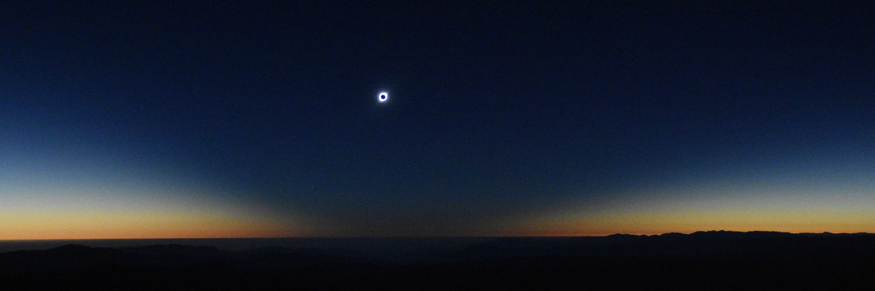 the sun covered by the moon during an eclipse, set against a darkening dusky sky with a black flat horizon in the foreground