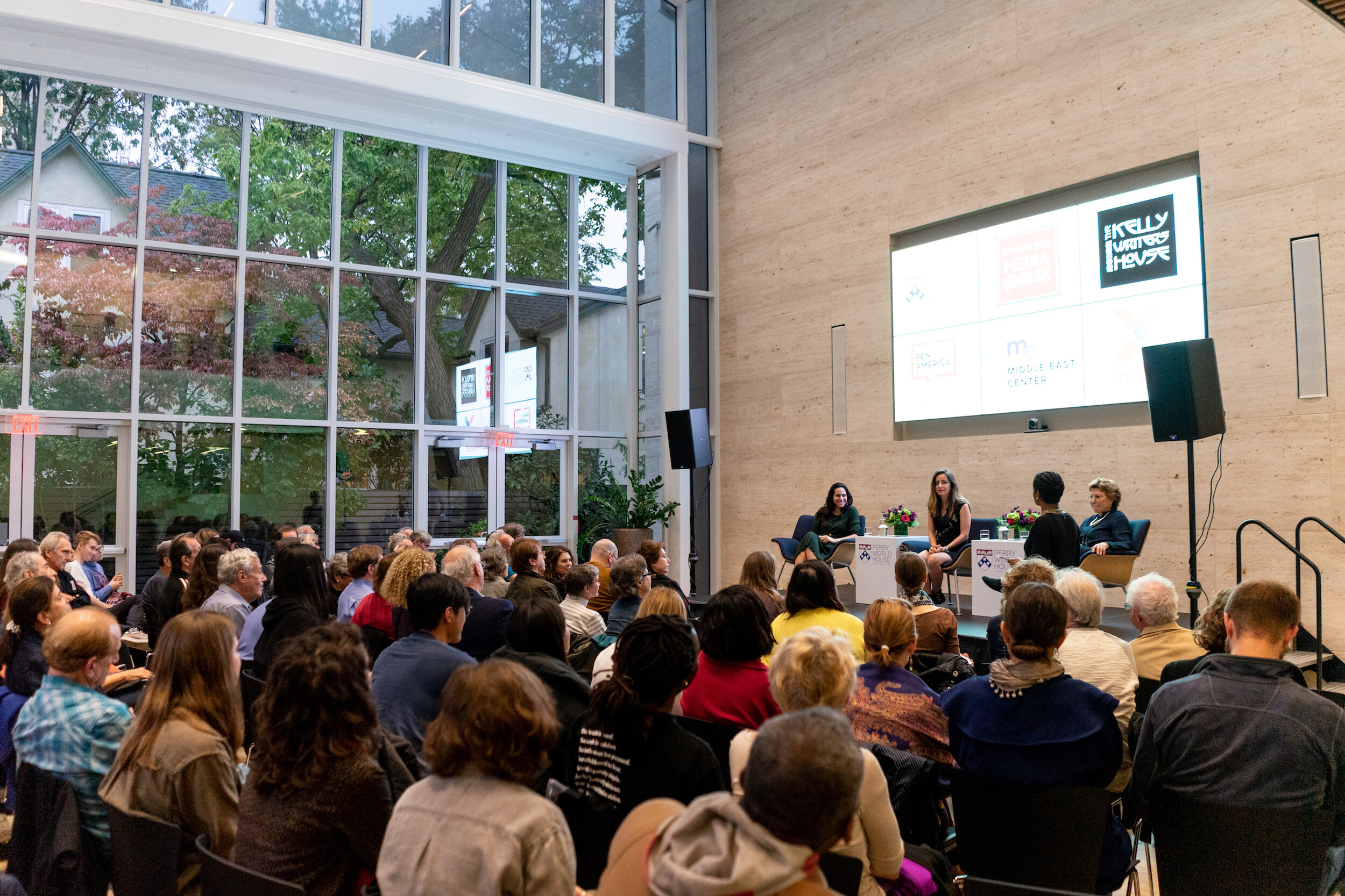 Three people sitting on stage in front of an audience of dozens of people. 