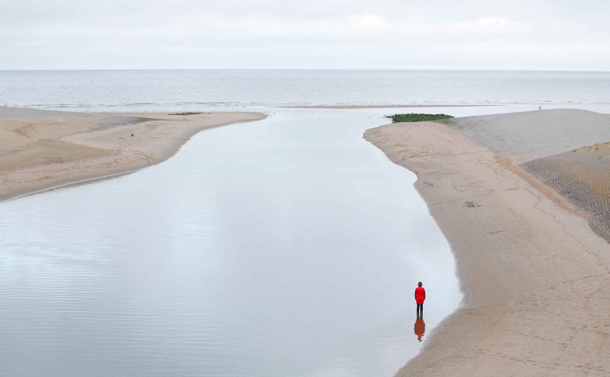 Person in red shirt stands in water looking out at the vast sea