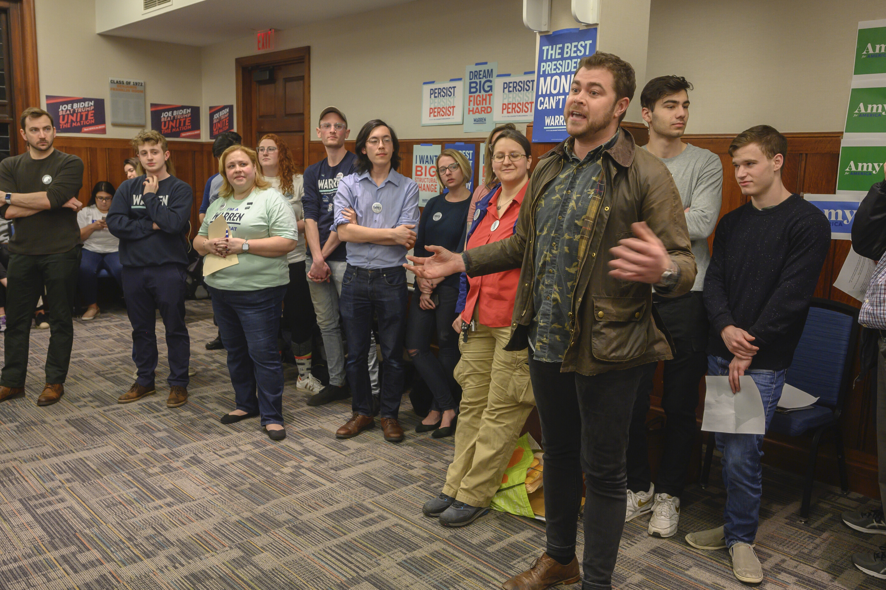 A group of people standing along the edge of a room, with political banners behind them.