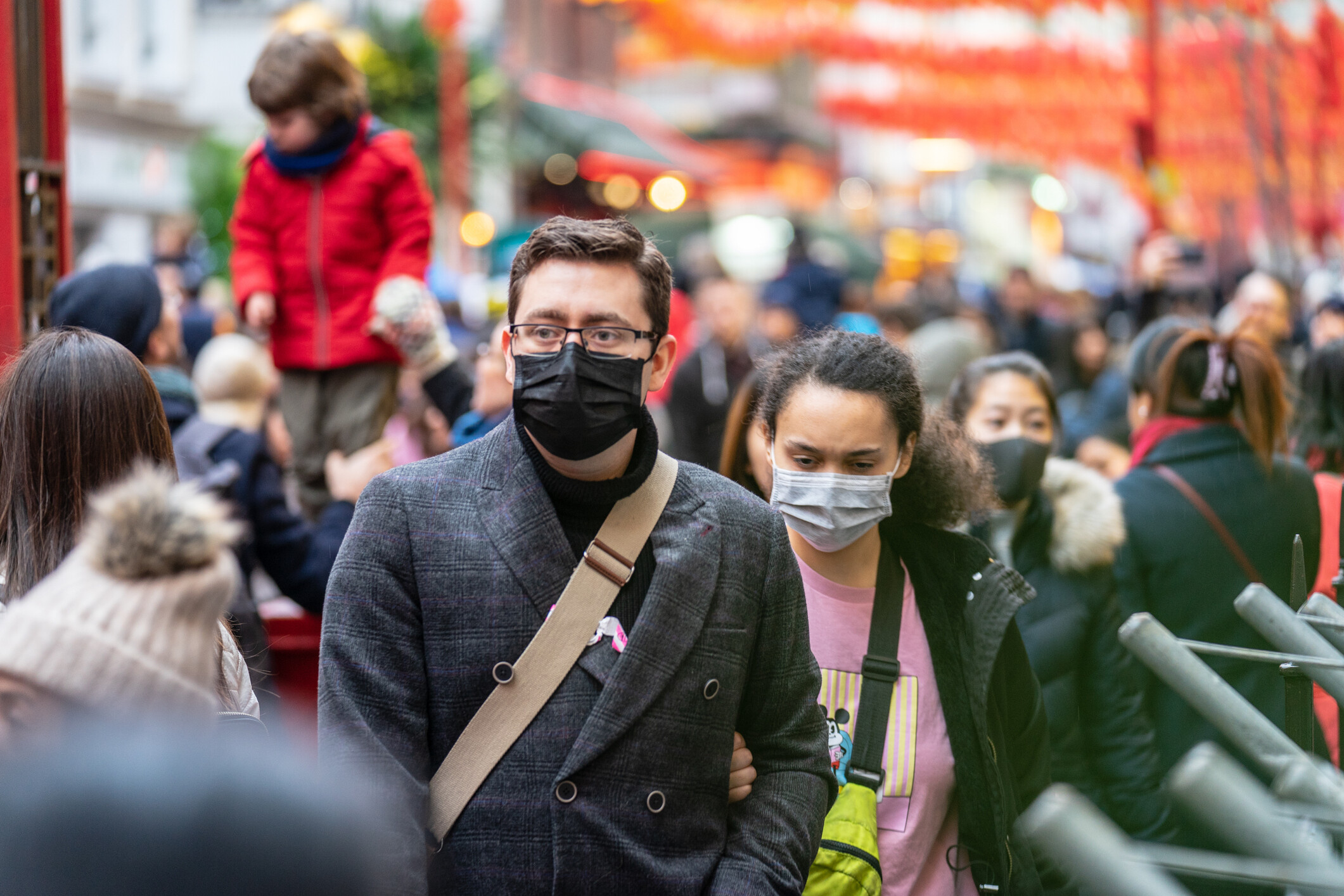 Groups of people walk in a crowd wearing masks but not social distancing.