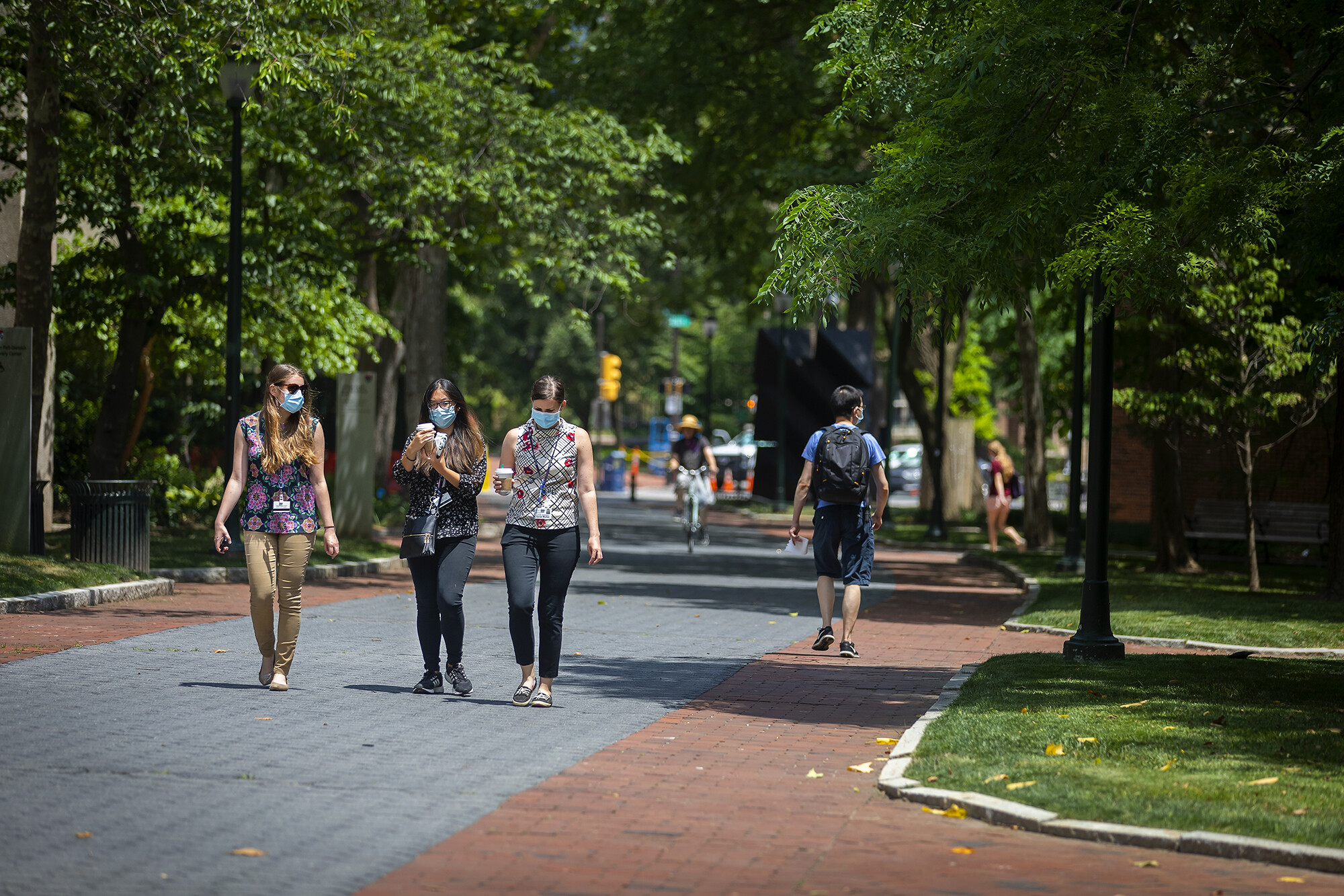 a group of people walking outside on campus while wearing masks