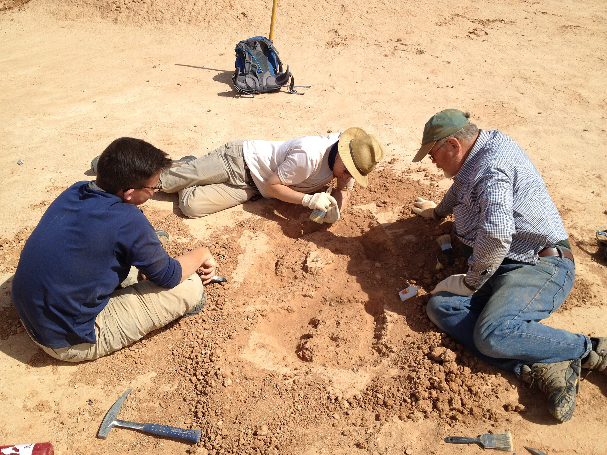 Three people on the dirt ground excavating in the dirt.