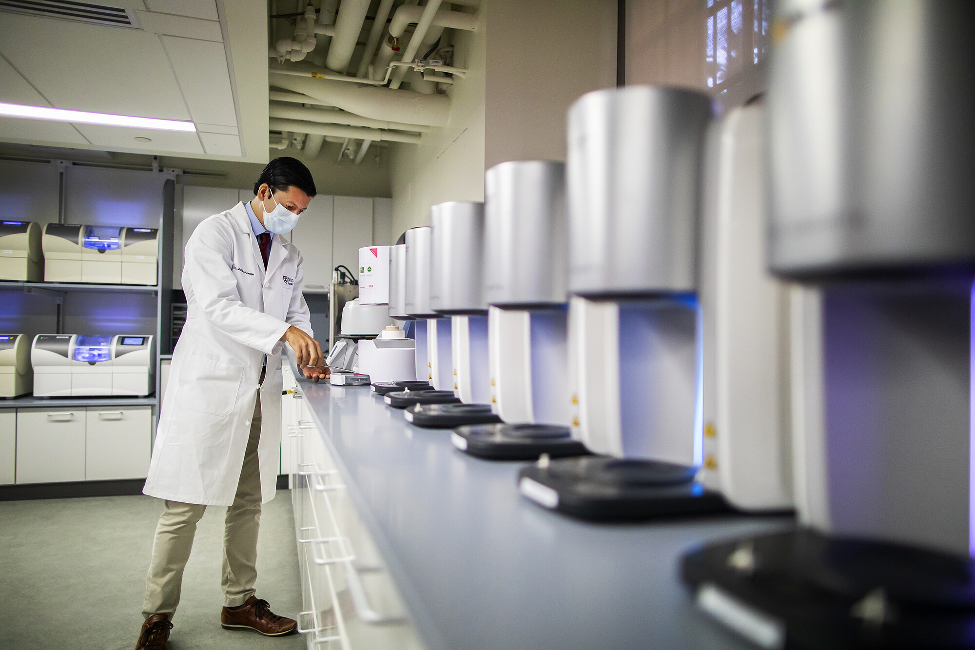 Person standing in a dental lab amongst many identical machines on a surface.