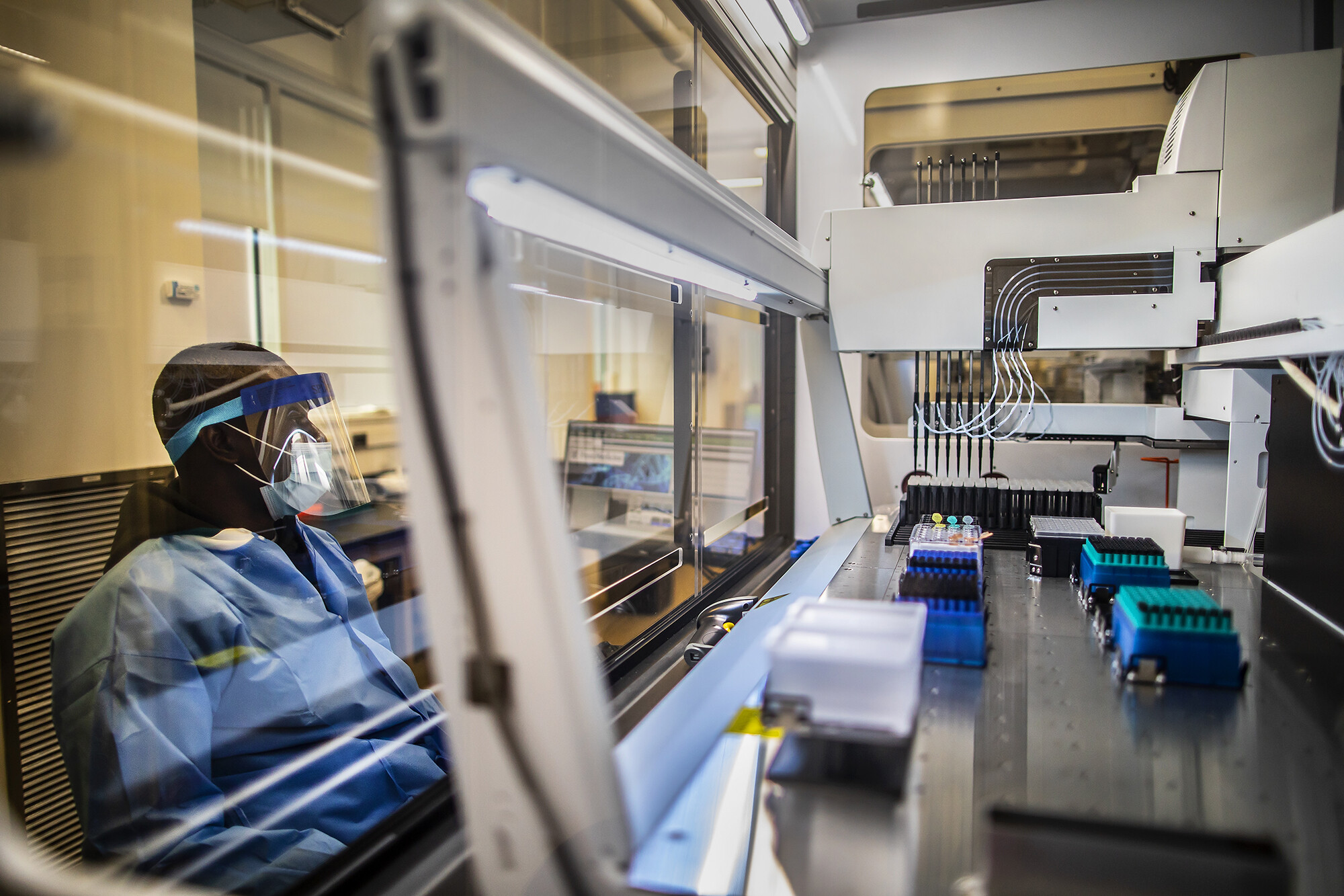 a person looking at a robotic pipetting machine on the other side of a glass partition