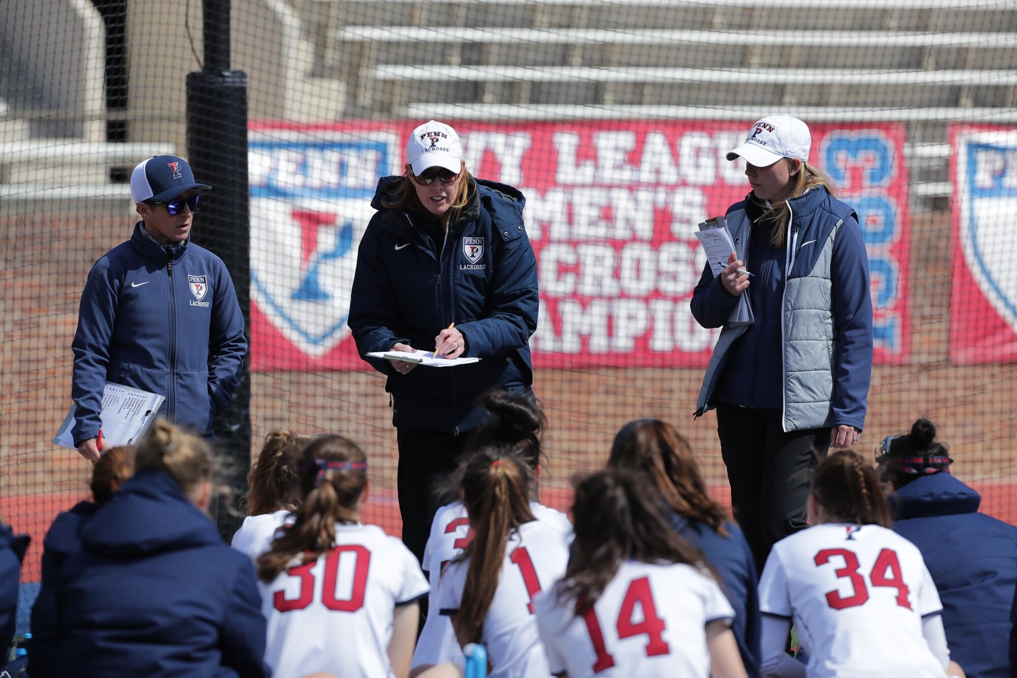 Coach Corbett speaks to her players, who are huddled on the ground in front of her.