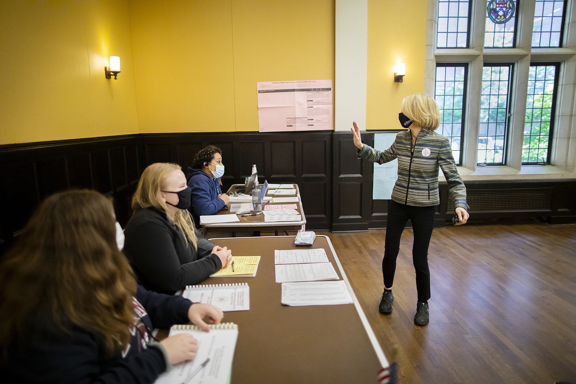 Amy Gutmann waves to three masked poll workers seated at desks in Houston Hall.