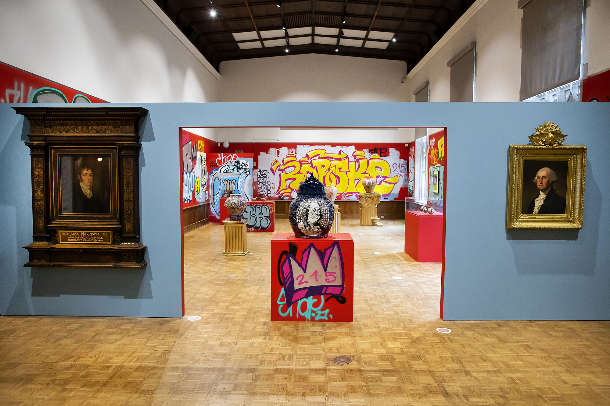 Art gallery with two formal portraits on one side of the wall and graffiti on the other