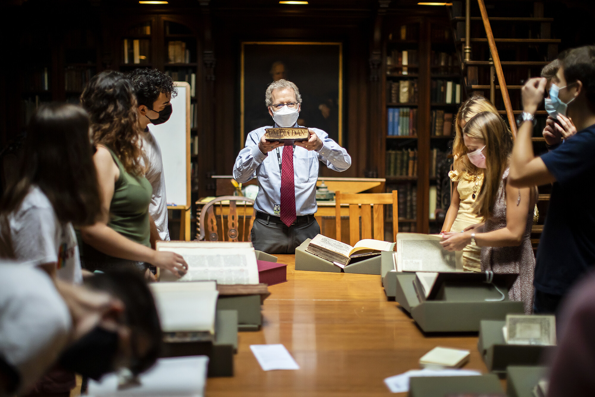 man holds a book up horizontally in front of a class
