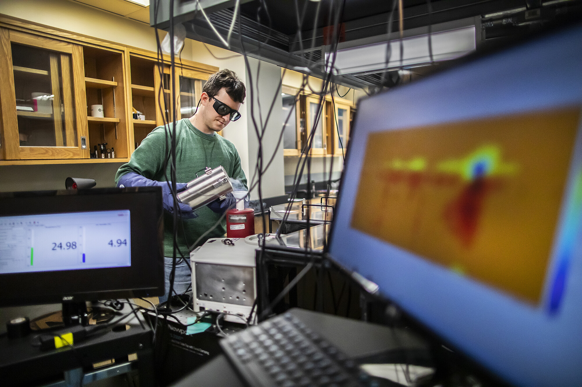 Student performs chemical research in lab, framed by computer screens and other equipment.