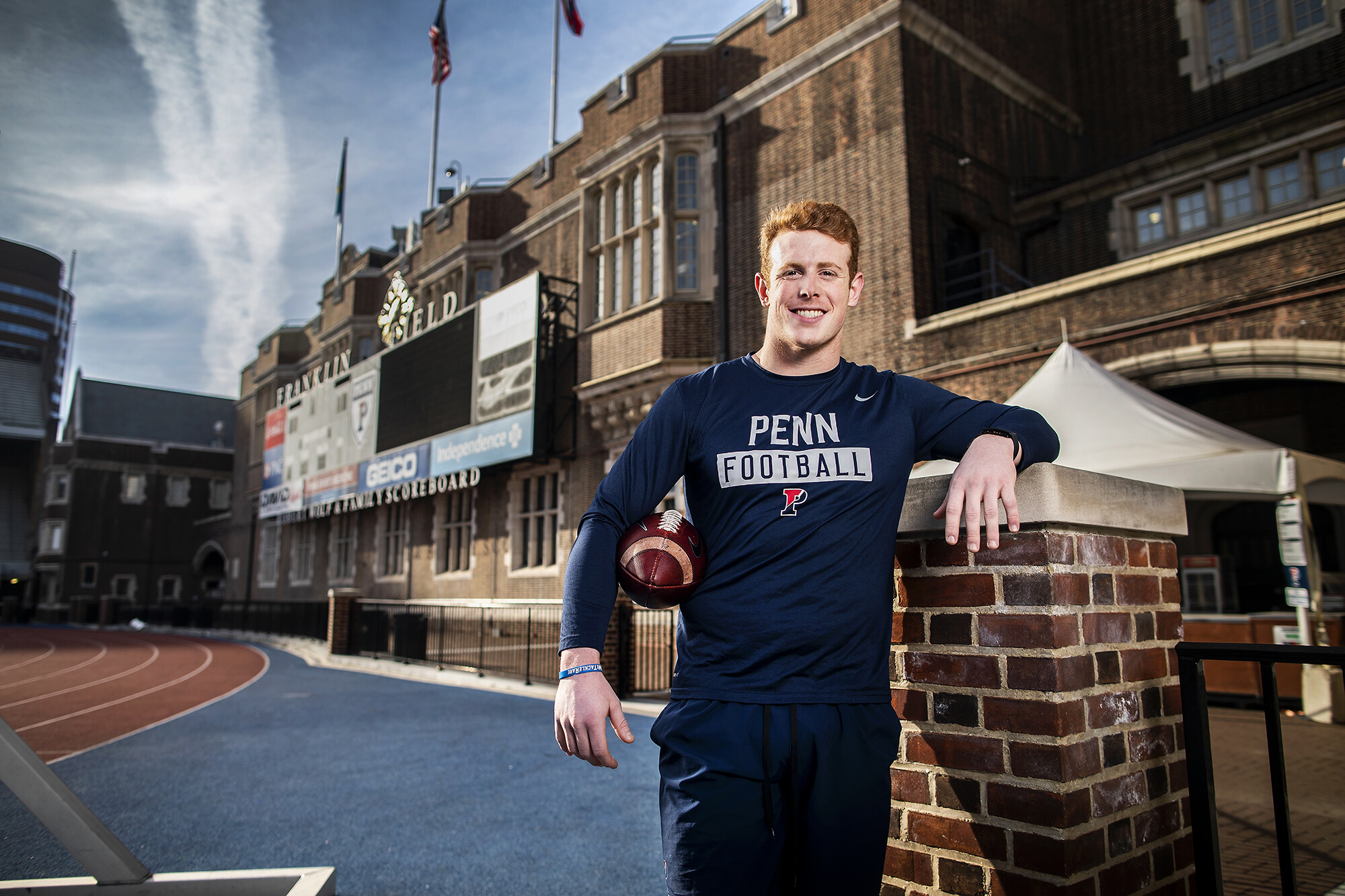O'Neill leans up against the wall at Franklin Field while holding a football.