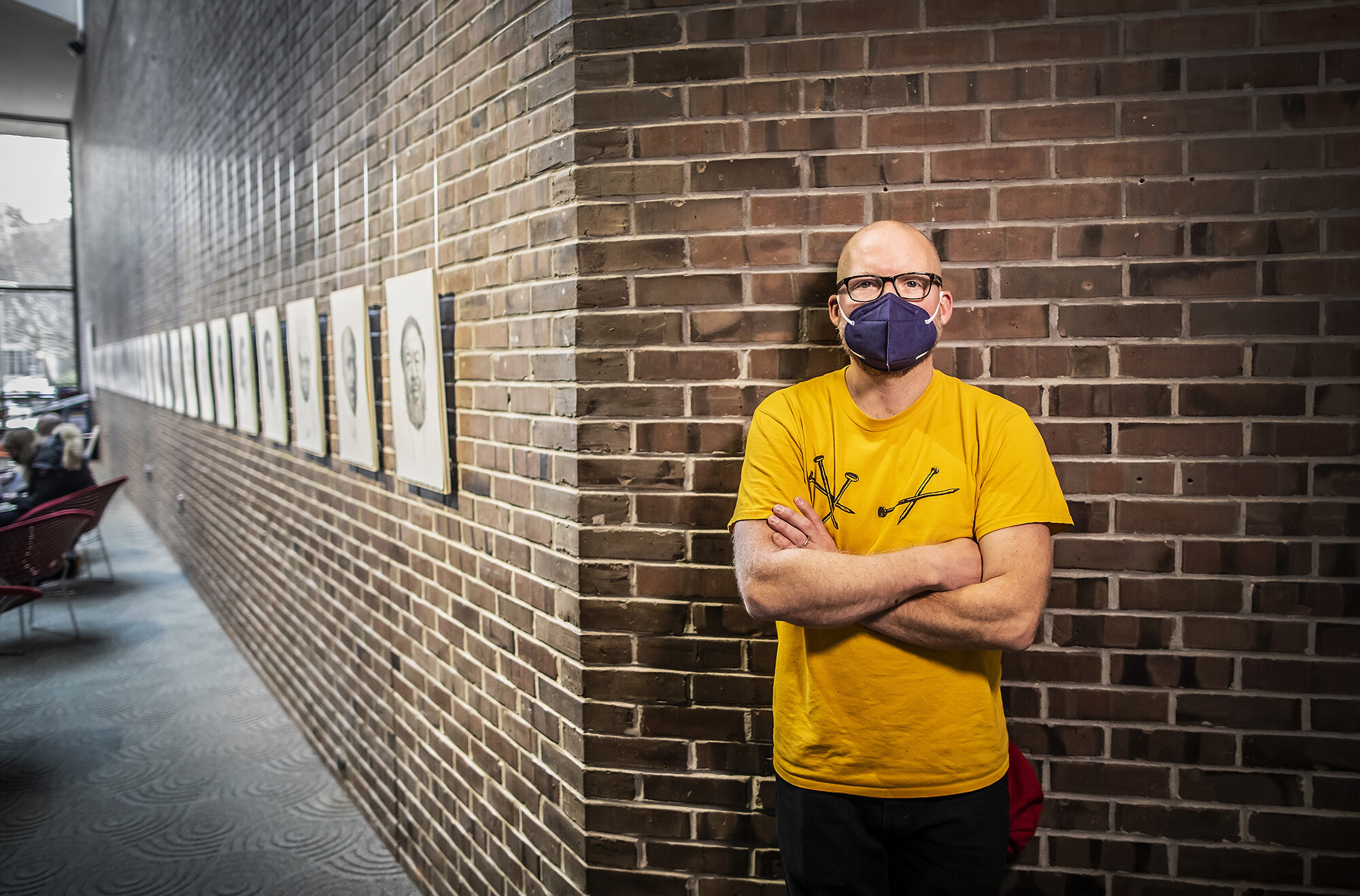 Mark Stockton leans against brick wall on corner from lineup of portraits