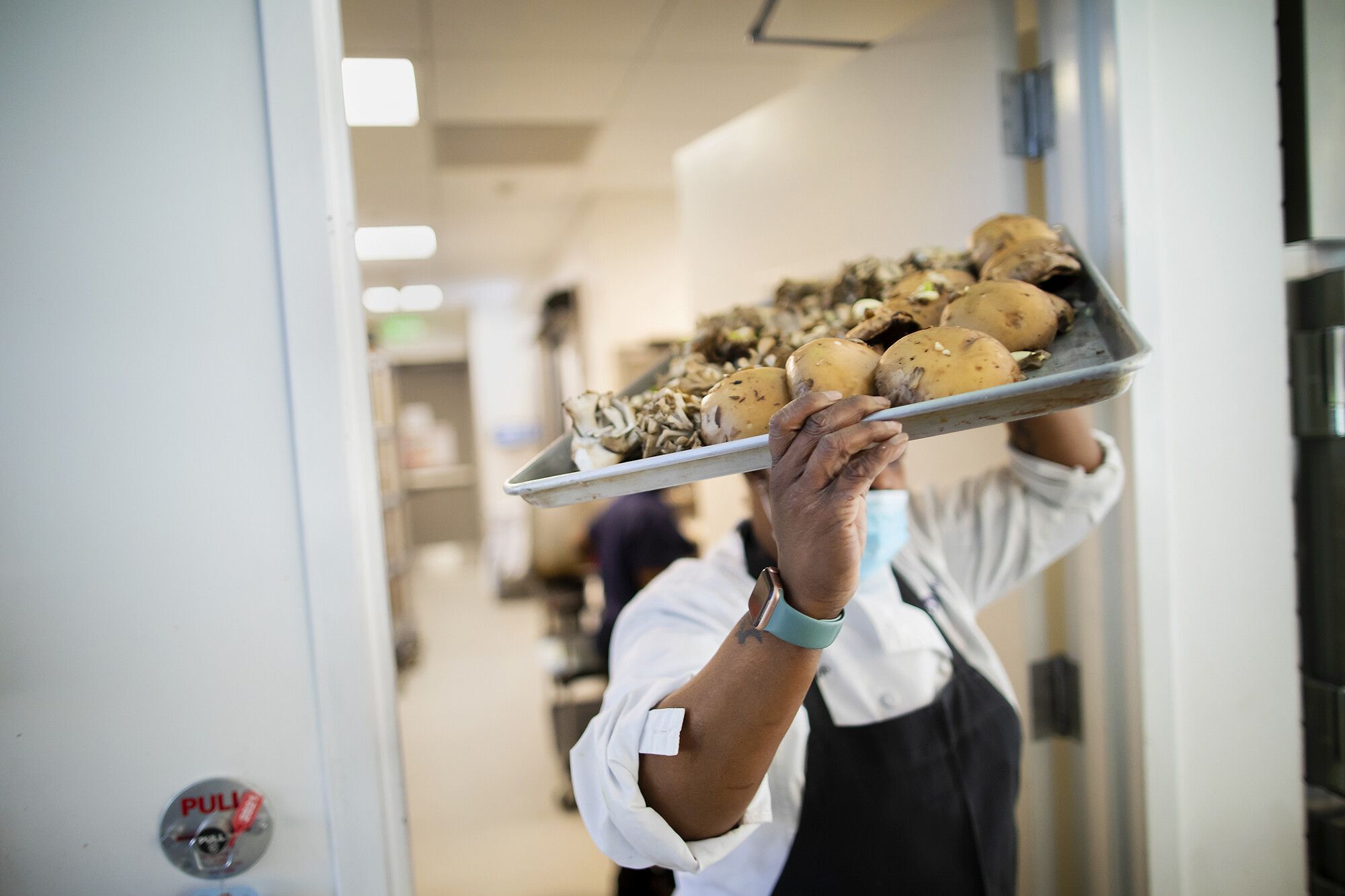 A person carrying a tray of mushrooms through a door. The person is holding the tray on their head.