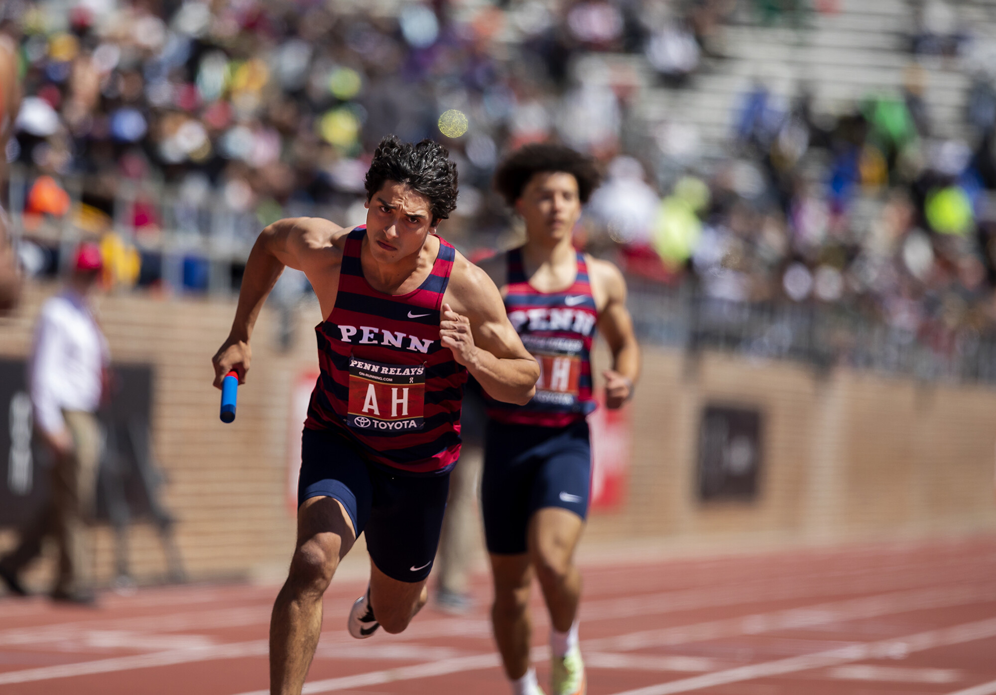 A runner holding a baton runs on a track.