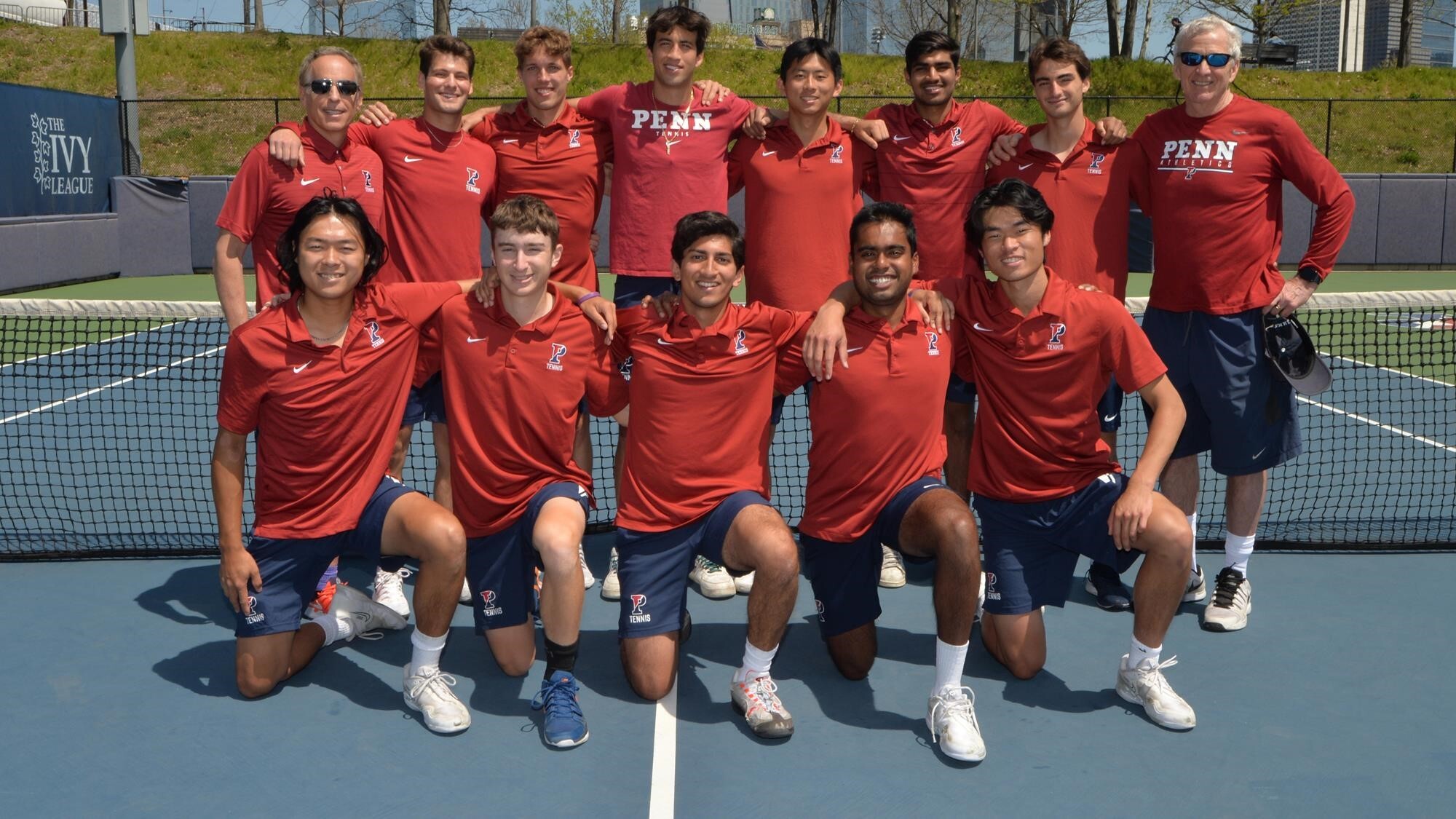 Tennis players pose for a group shot on the tennis court.