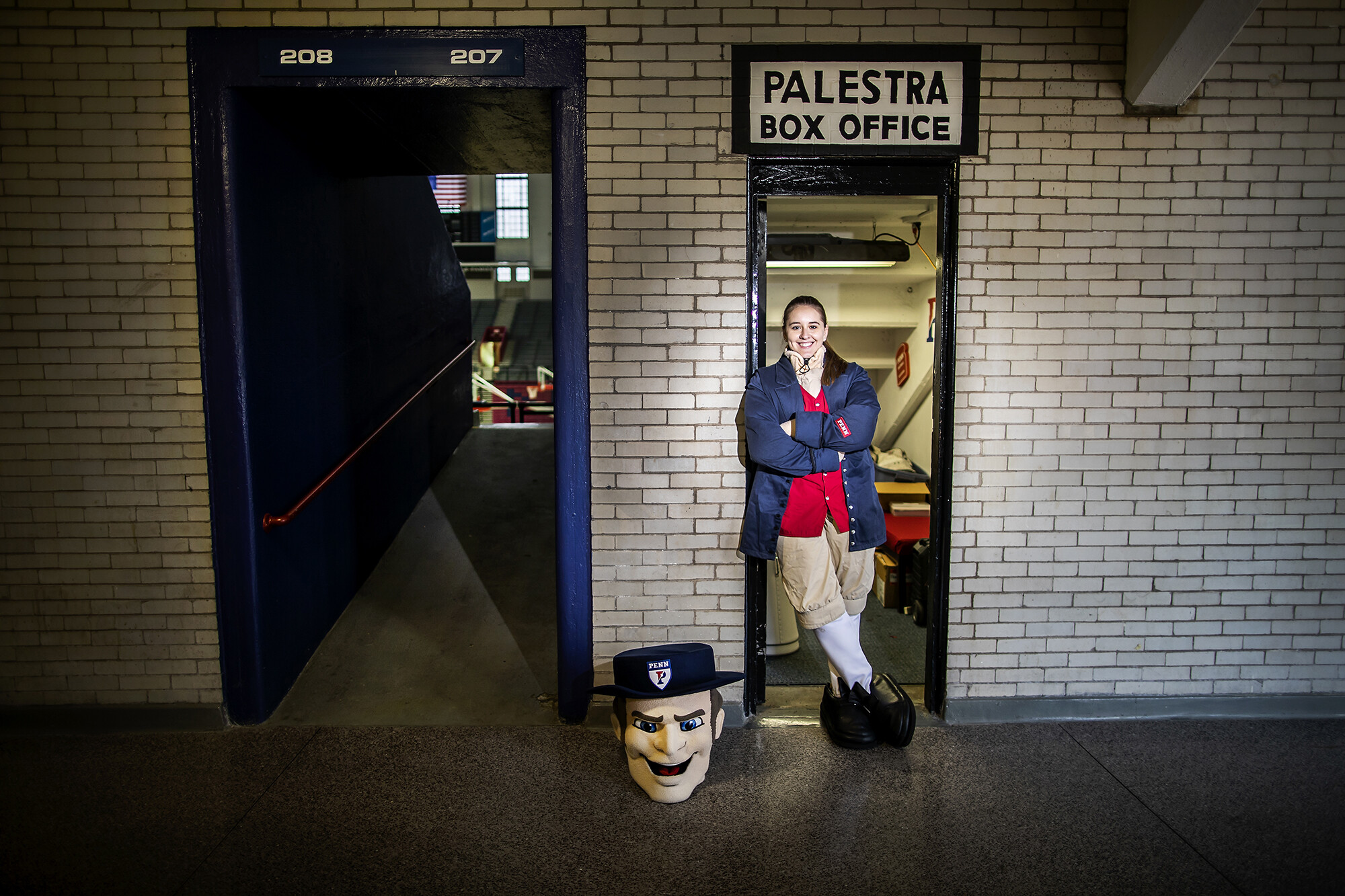 Sophia Zehler in her Quaker mascot costume in the doorway of the Palestra Box Office.