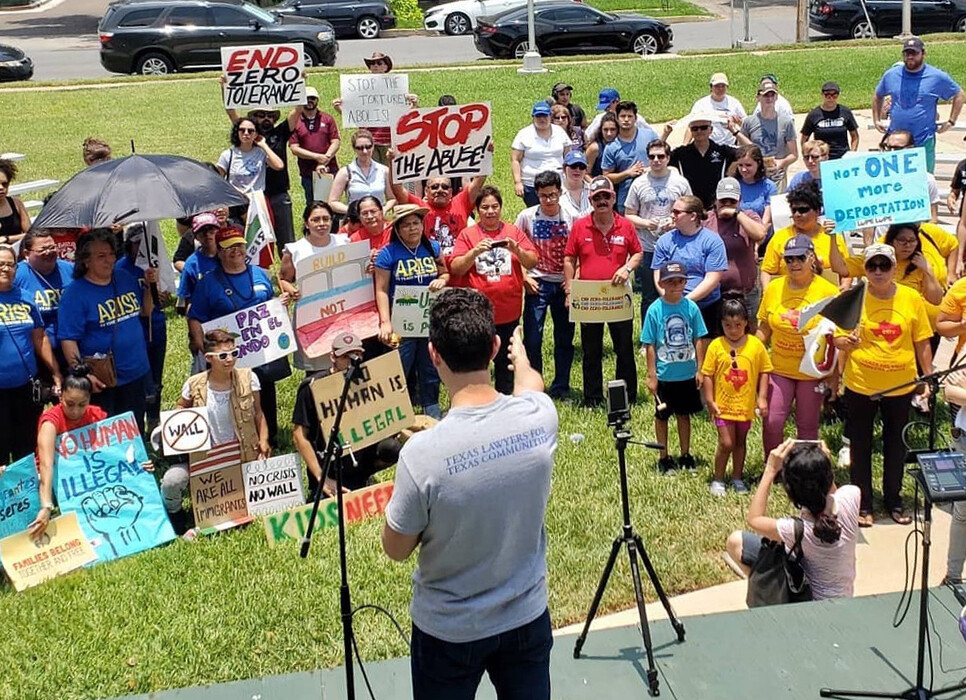 Efrén Olivares speaks to a crowd of people holding signs that say "end zero tolerance," "no human is illegal," and "not one more deportation."