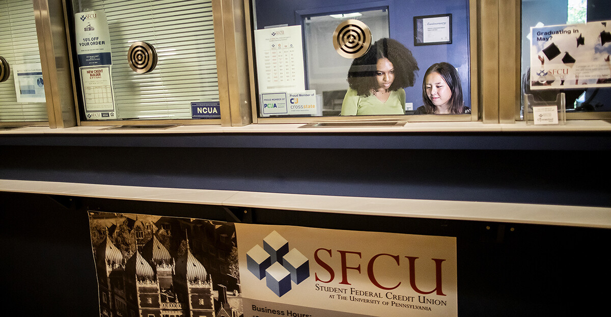 Two student workers behind a bank counter window.