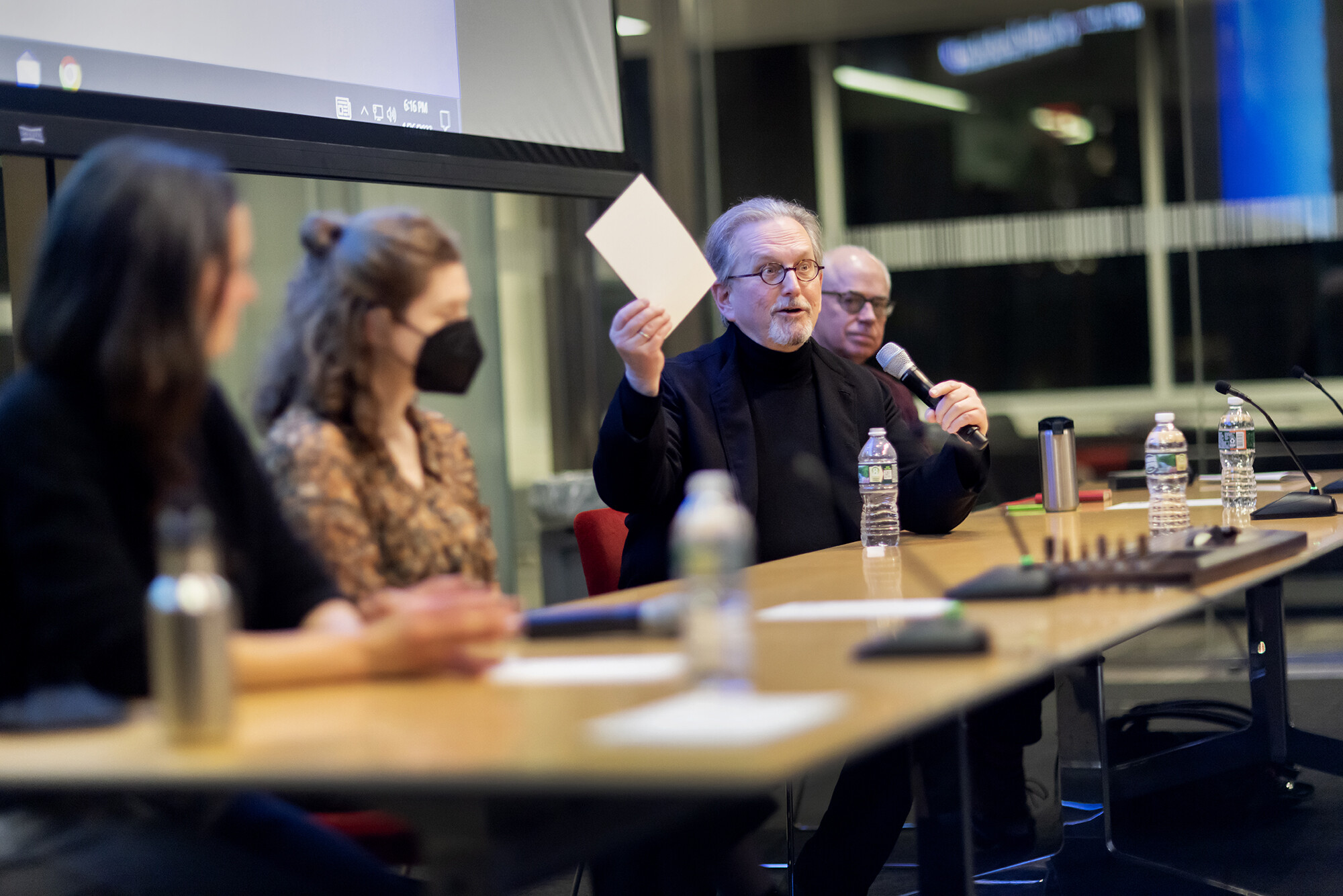 Four people sitting at a table, one holding a microphone and a piece of paper in the air