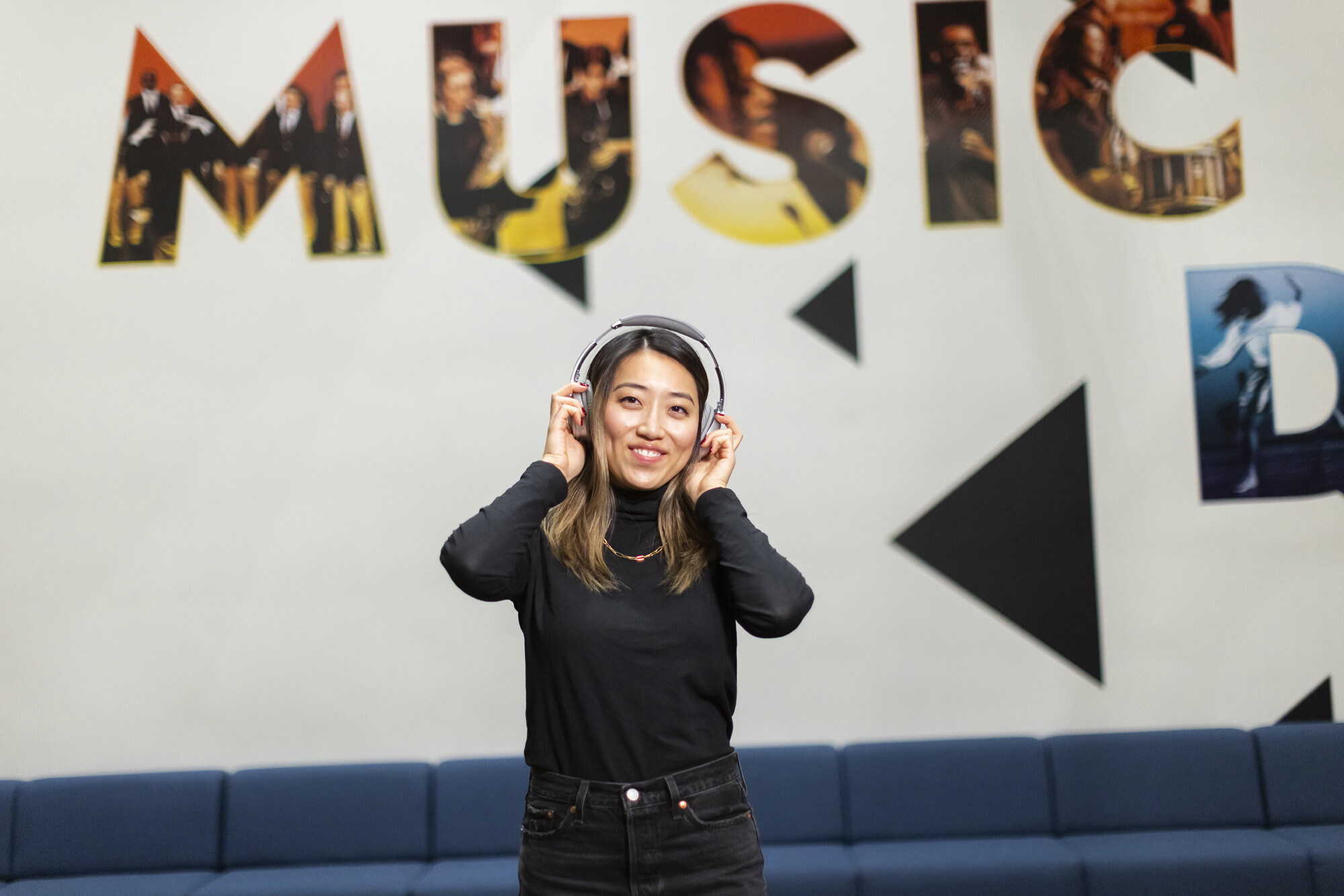 Person holding headphones in front of mural that reads 'Music'