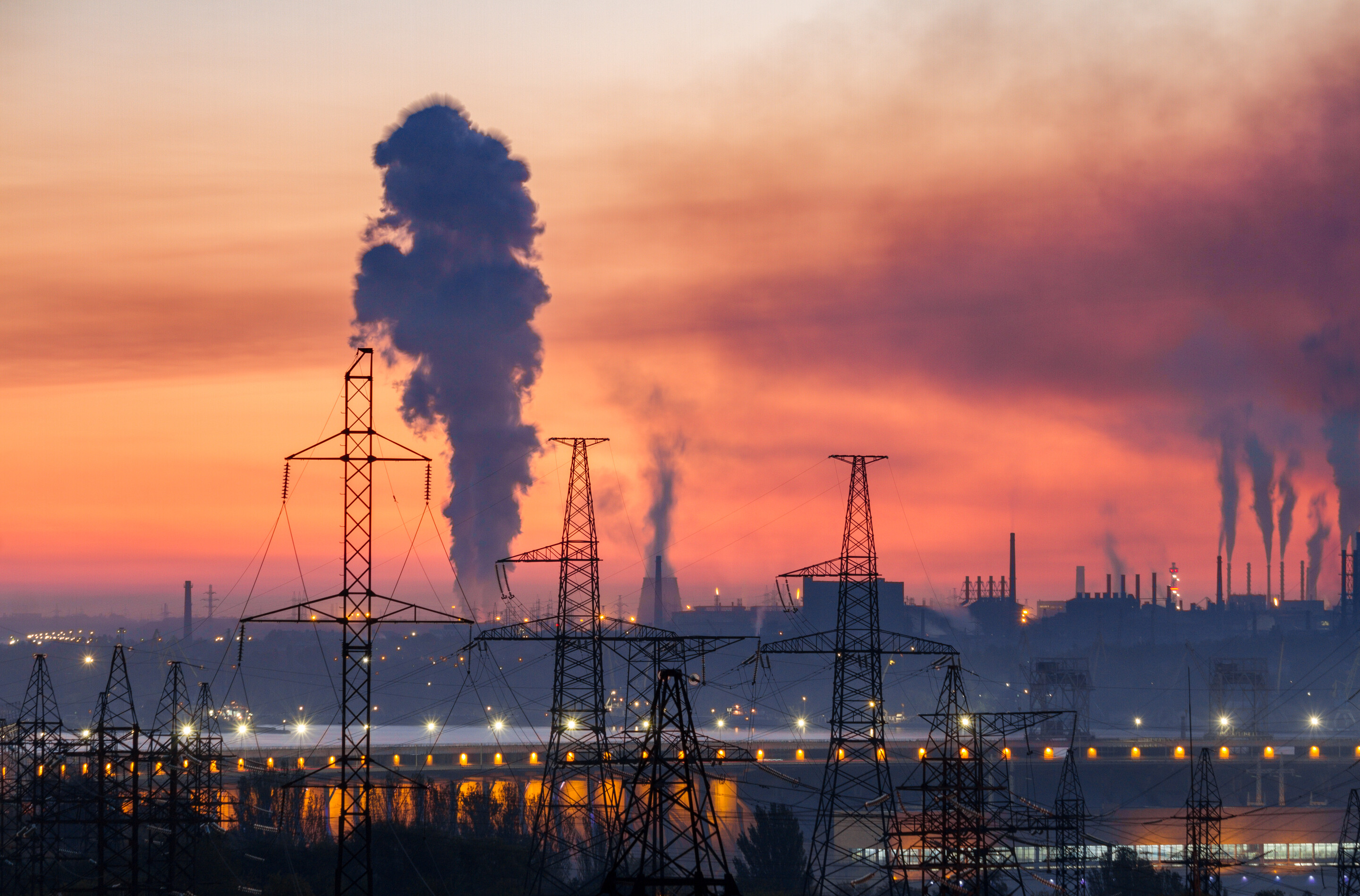 Industrial landscape with electric power lines, hydroelectric dam and metallurgical plants with smoke in the sky.
