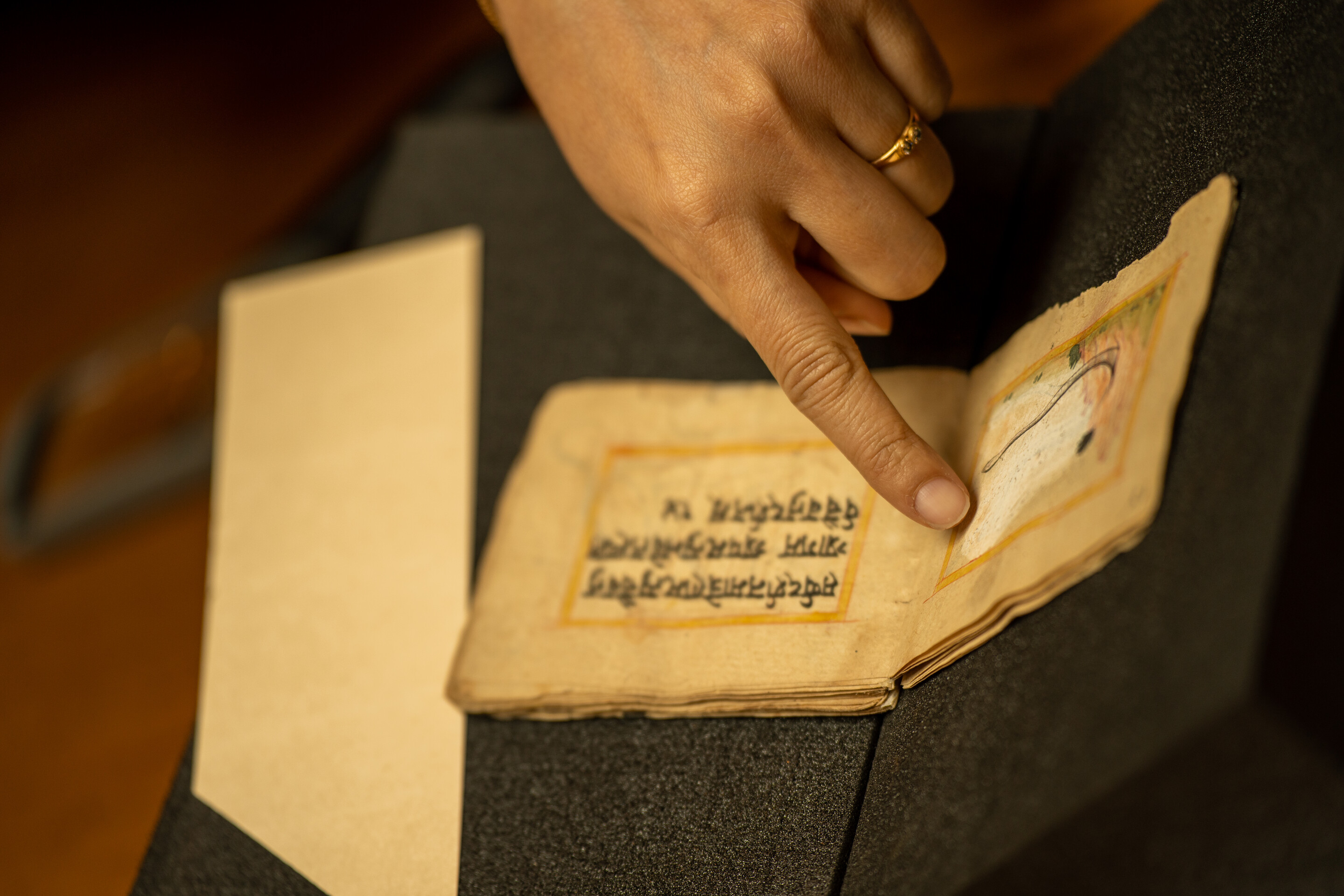 A finger points to an illustration in a small, antique book.