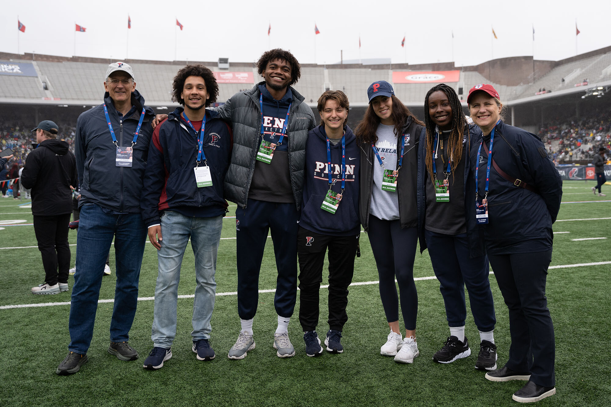 President Liz Magill, right, enjoys the Penn Relays with her husband Leon Szeptycki, left, and Penn students.