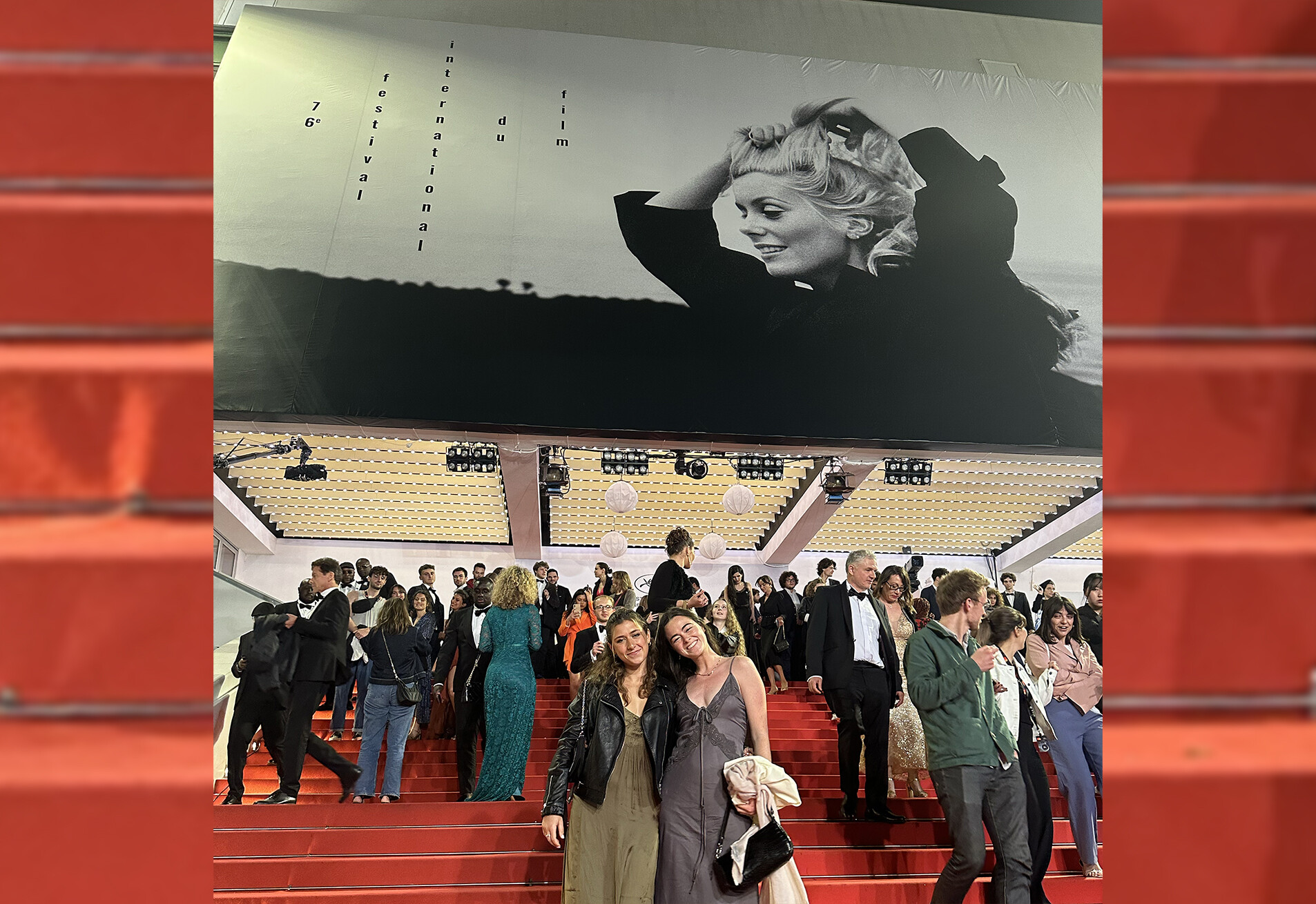 two students standing on the red carpet steps with many people behind them