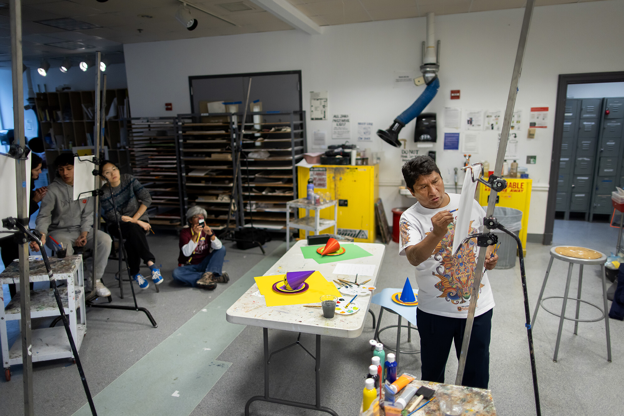 Roberto Mamani Mamani paints on an easel-mounted canvas while students look on 