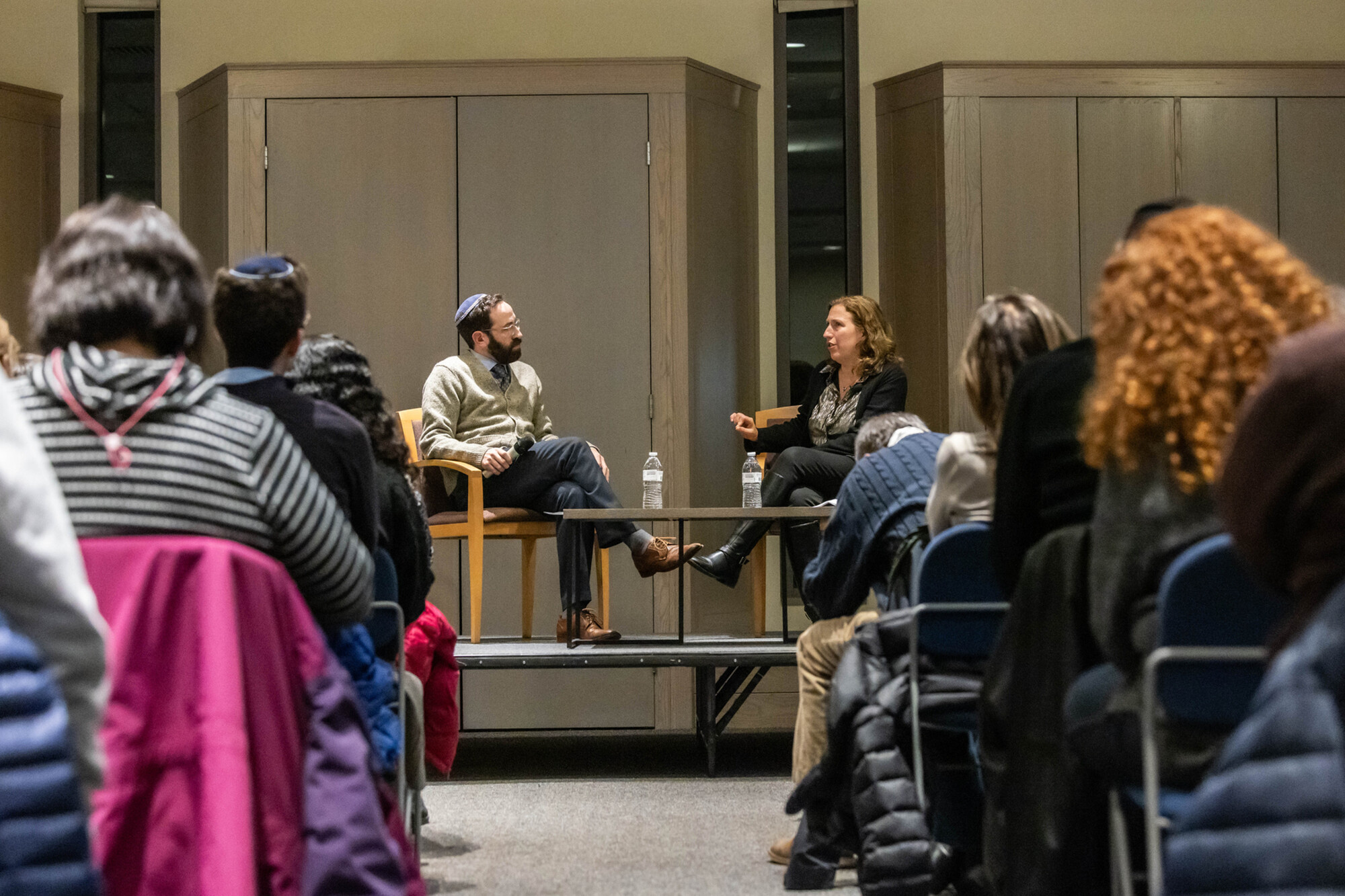 Dara Horn sitting on a platform talking with Rabbi Gabe Greenberg in front of an audience sitting in chairs