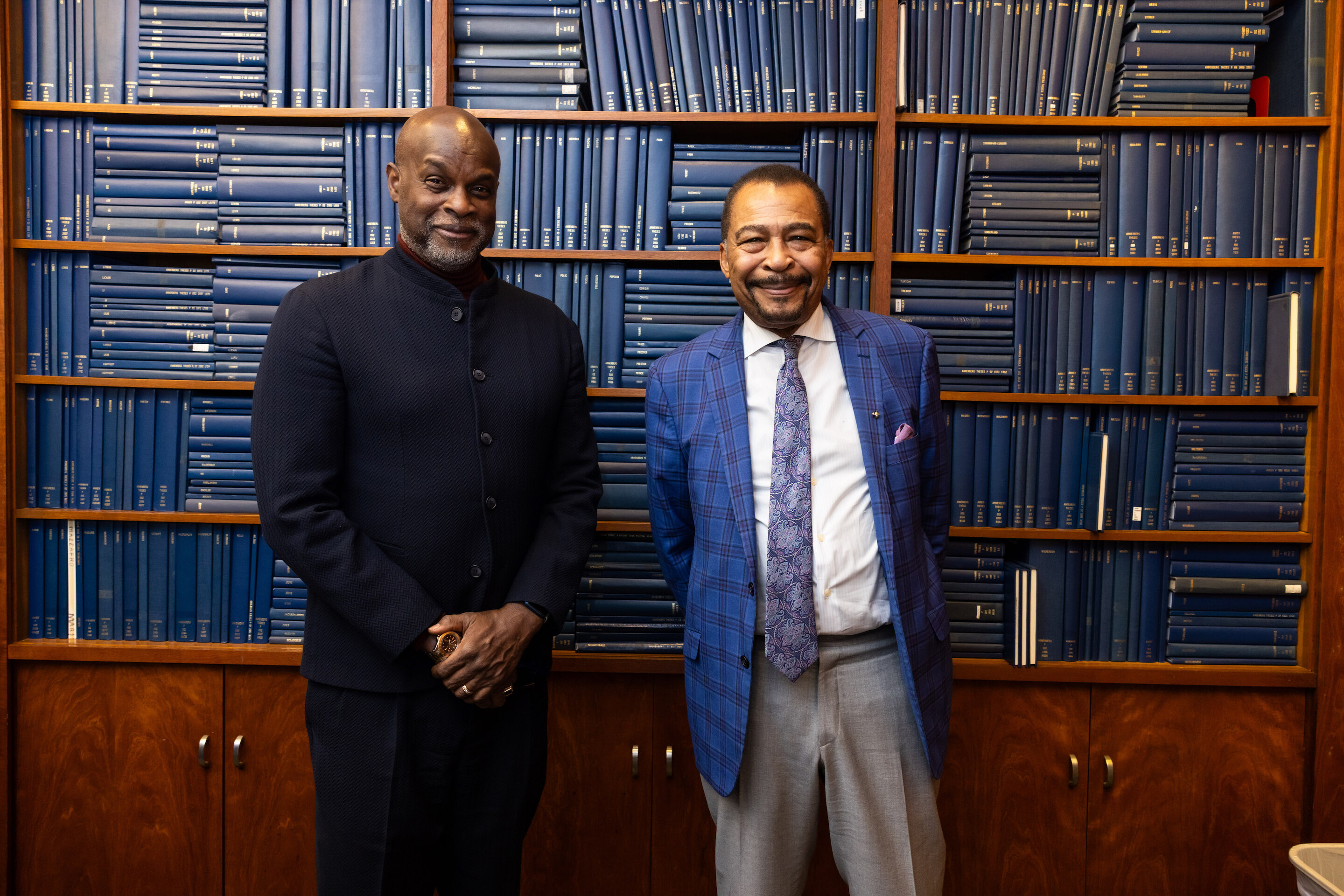 Tukufu Zuberi and Aldon Morris against a backdrop of blue hardback books stacked vertically and horizontally in a bookcase