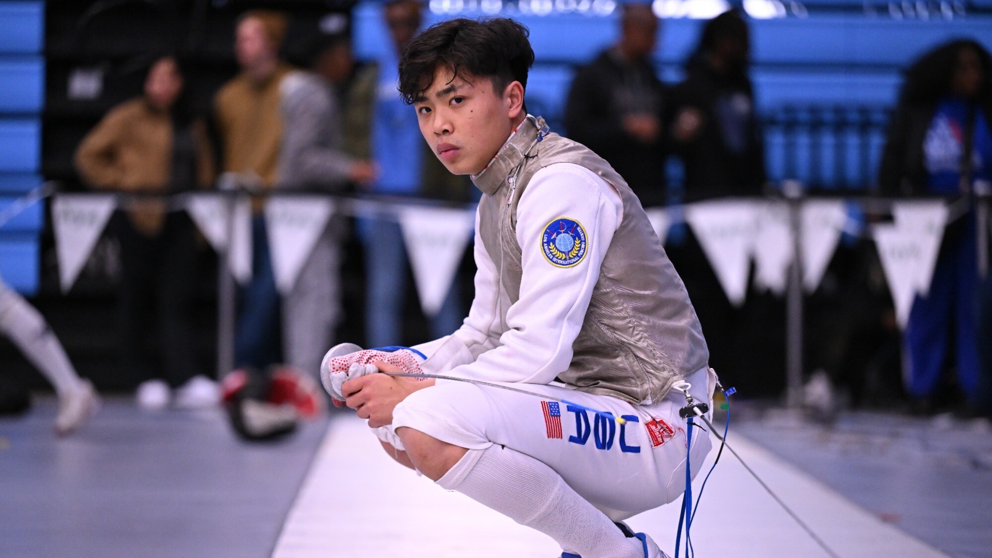 Bryce Louie kneels down with his fencing foil sword.