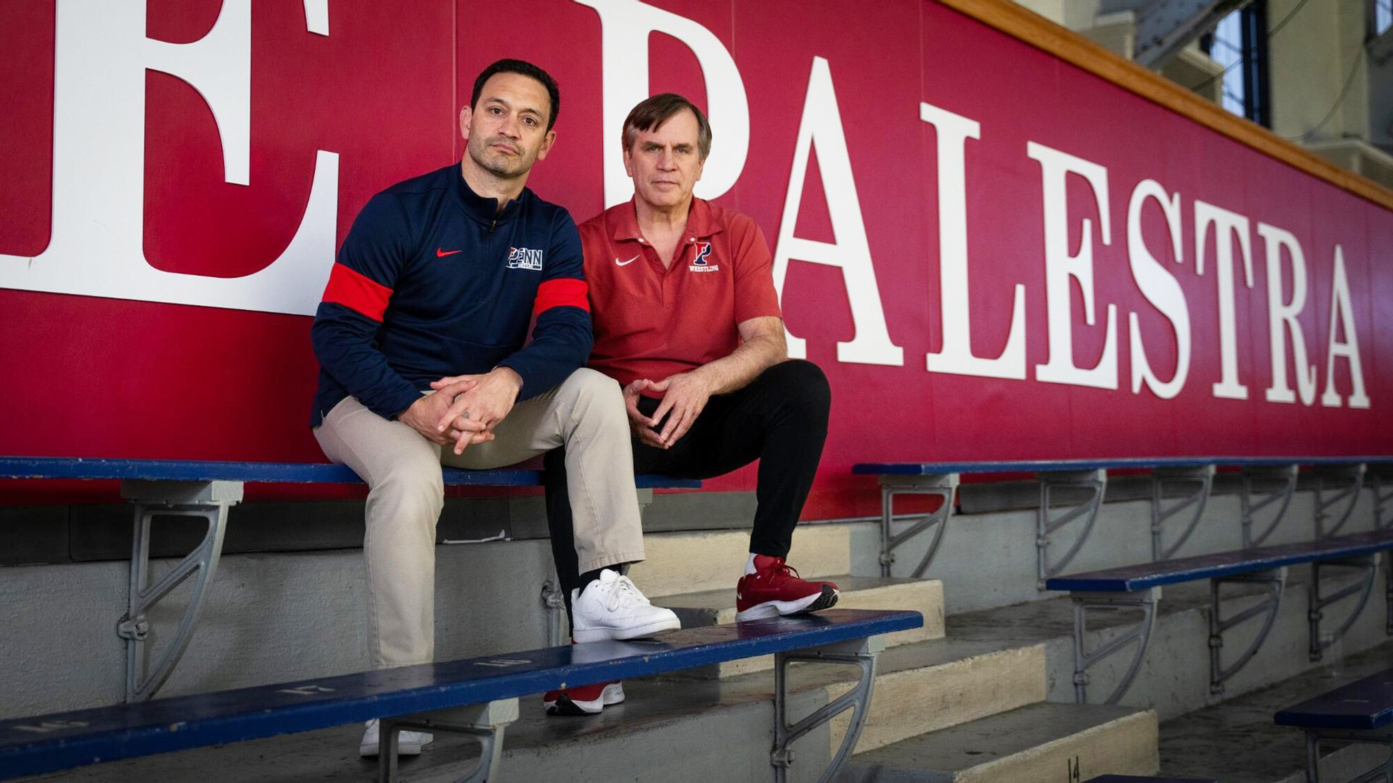Matt Valenti, left, and Roger Reina sit on a blue bleacher bench inside the Palestra.