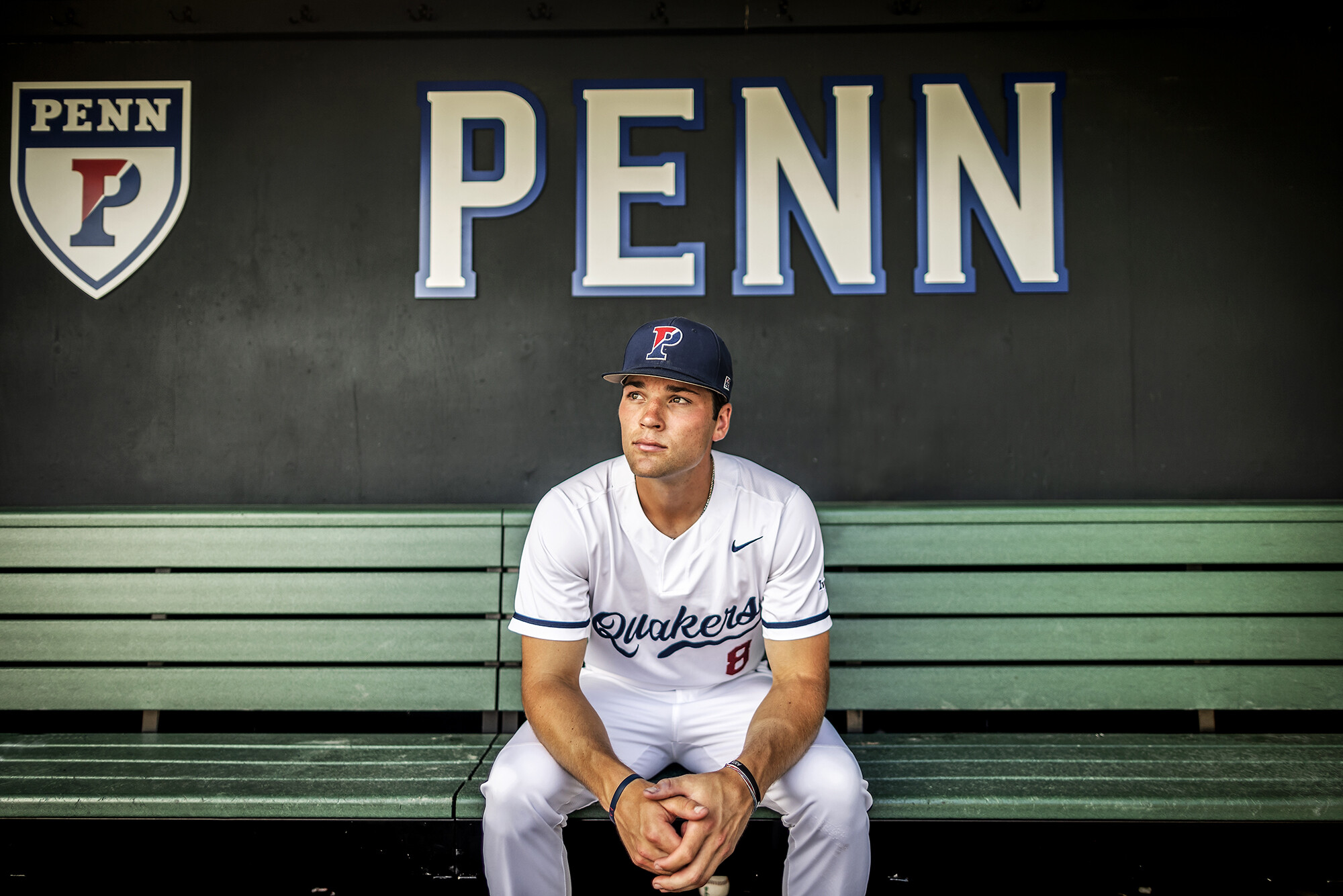 Wyatt Henseler sits in the dugout below a PENN sign.