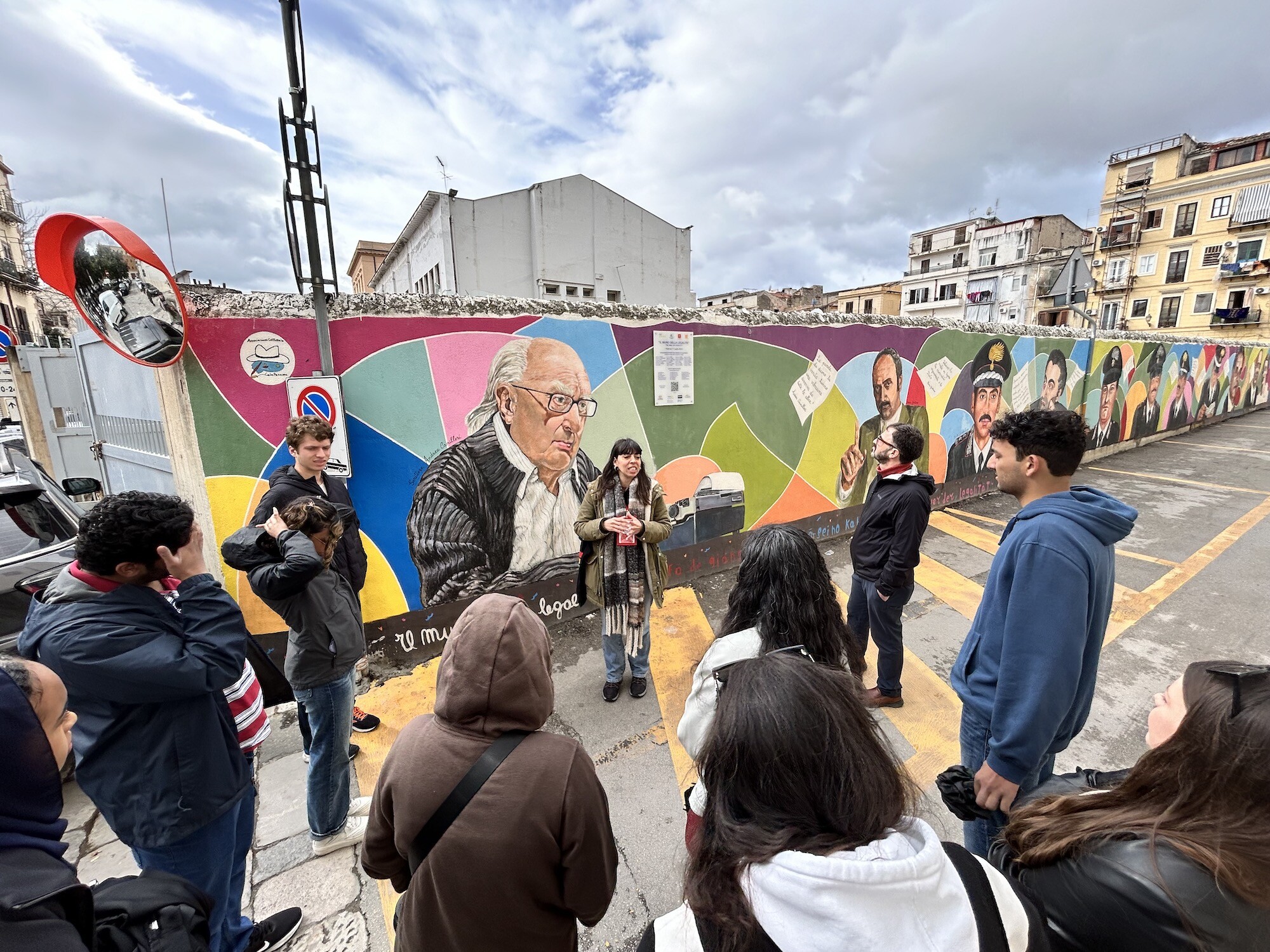 Students stand in front of a mural of anti-mafia workers in Palermo, Italy.